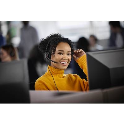 Eine Person sitzt lächelnd vor einem Computer und trägt ein Headset, möglicherweise in einem Kundenservice-Büro.