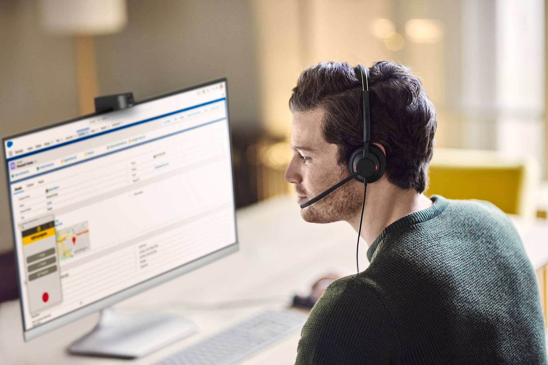 Ein Mann mit Headset sitzt vor einem Computerbildschirm, der eine Kundenservice-Software anzeigt, in einem modernen Büro.