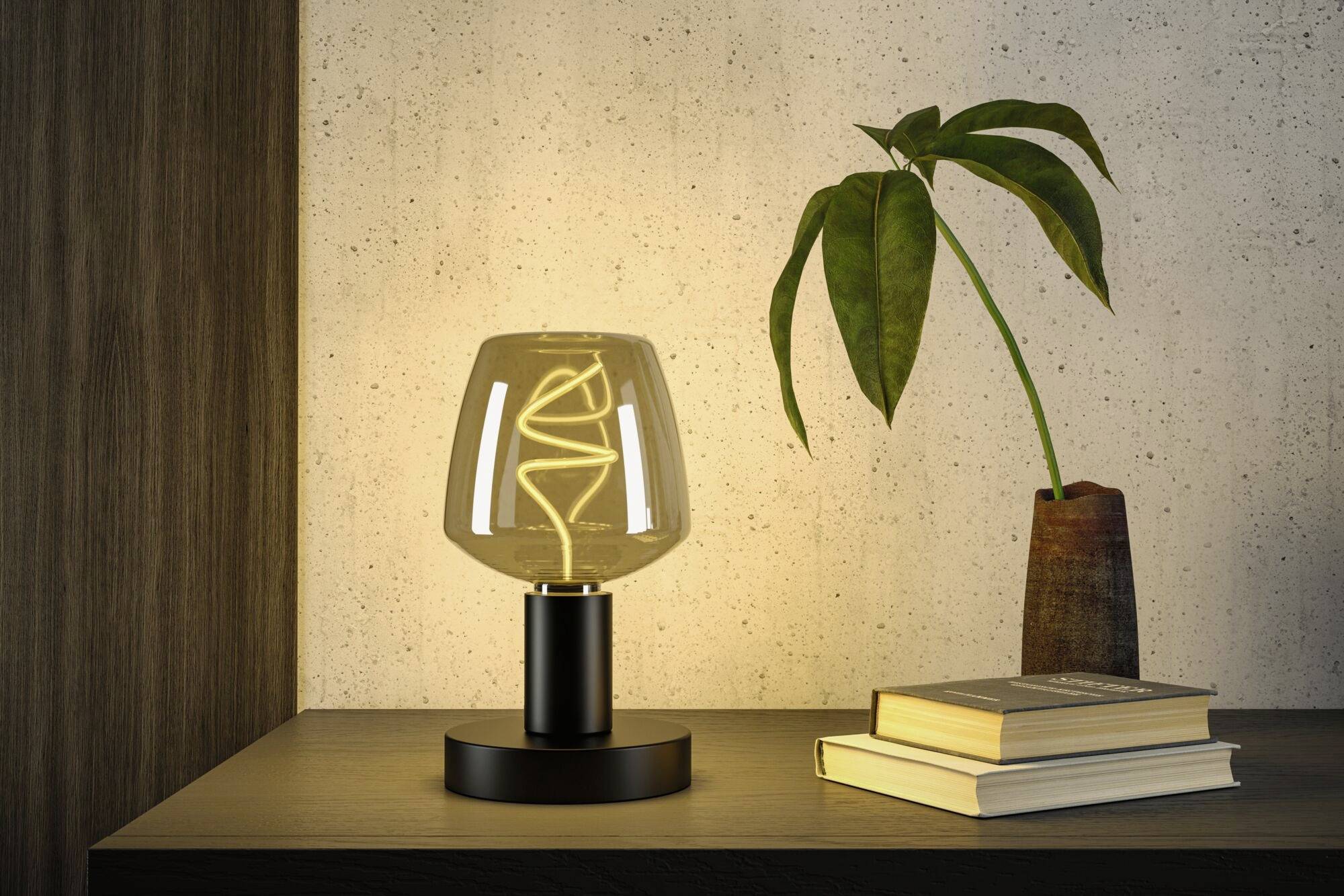 Eine stilvolle Tischlampe mit spiralförmigem Glühfaden leuchtet auf einem Holzregal. Daneben stehen gestapelte Bücher und eine Pflanze in einer Vase.