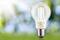 Glühbirne vor verschwommenem grünen Hintergrund, die Sonnenstrahlen reflektiert.