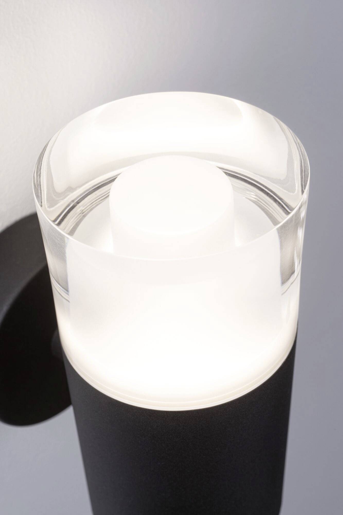 Eine moderne, zylindrische Wandleuchte aus Metall mit einem auffälligen, milchigen Glaszylinder, der weiches Licht ausstrahlt.