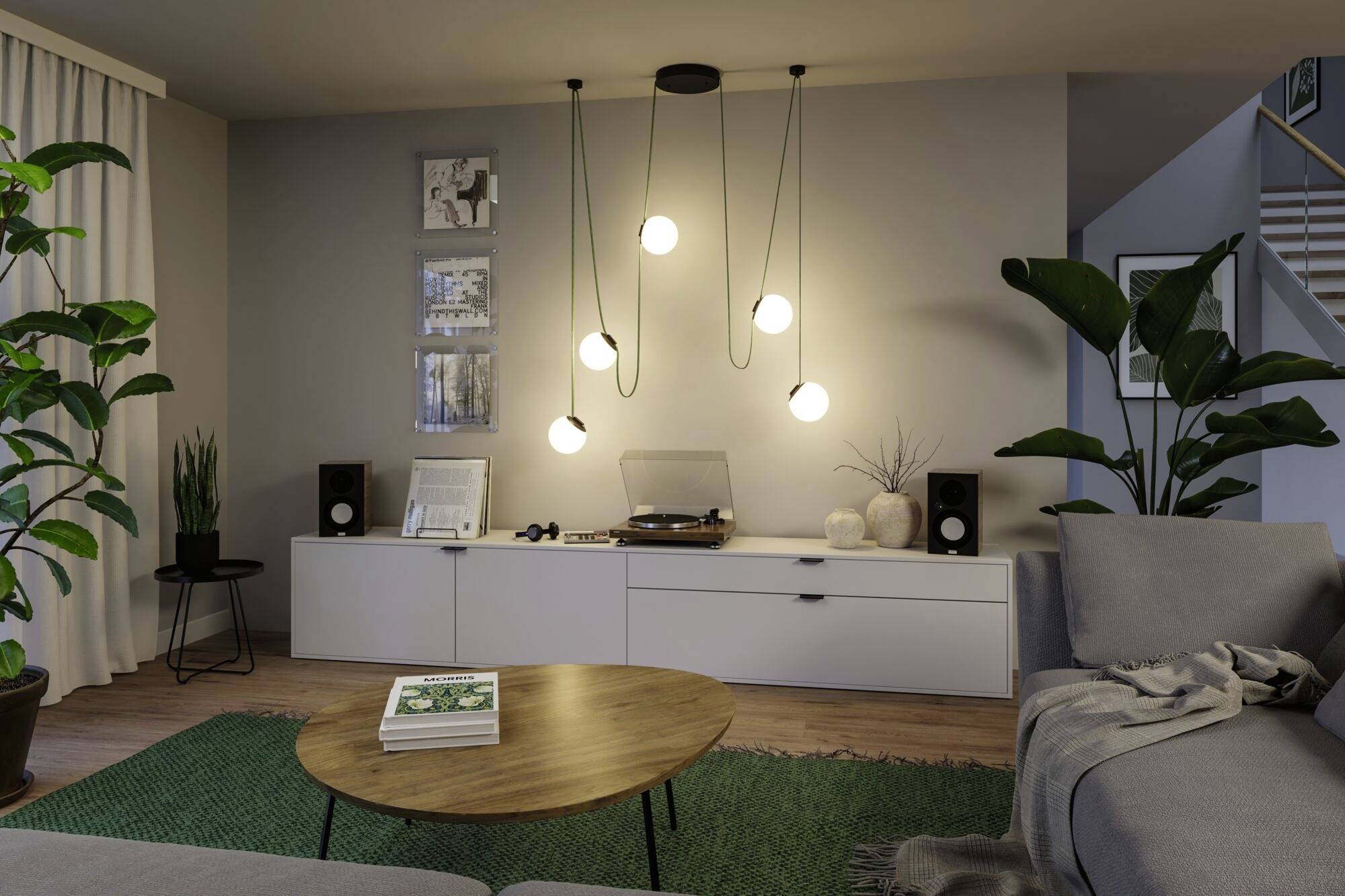 Ein Wohnzimmer mit modernen Möbeln: ein graues Sofa, runder Holztisch, grüne Pflanzen und hängende Lampen. An der Wand steht ein Sideboard mit Musikanlage.
