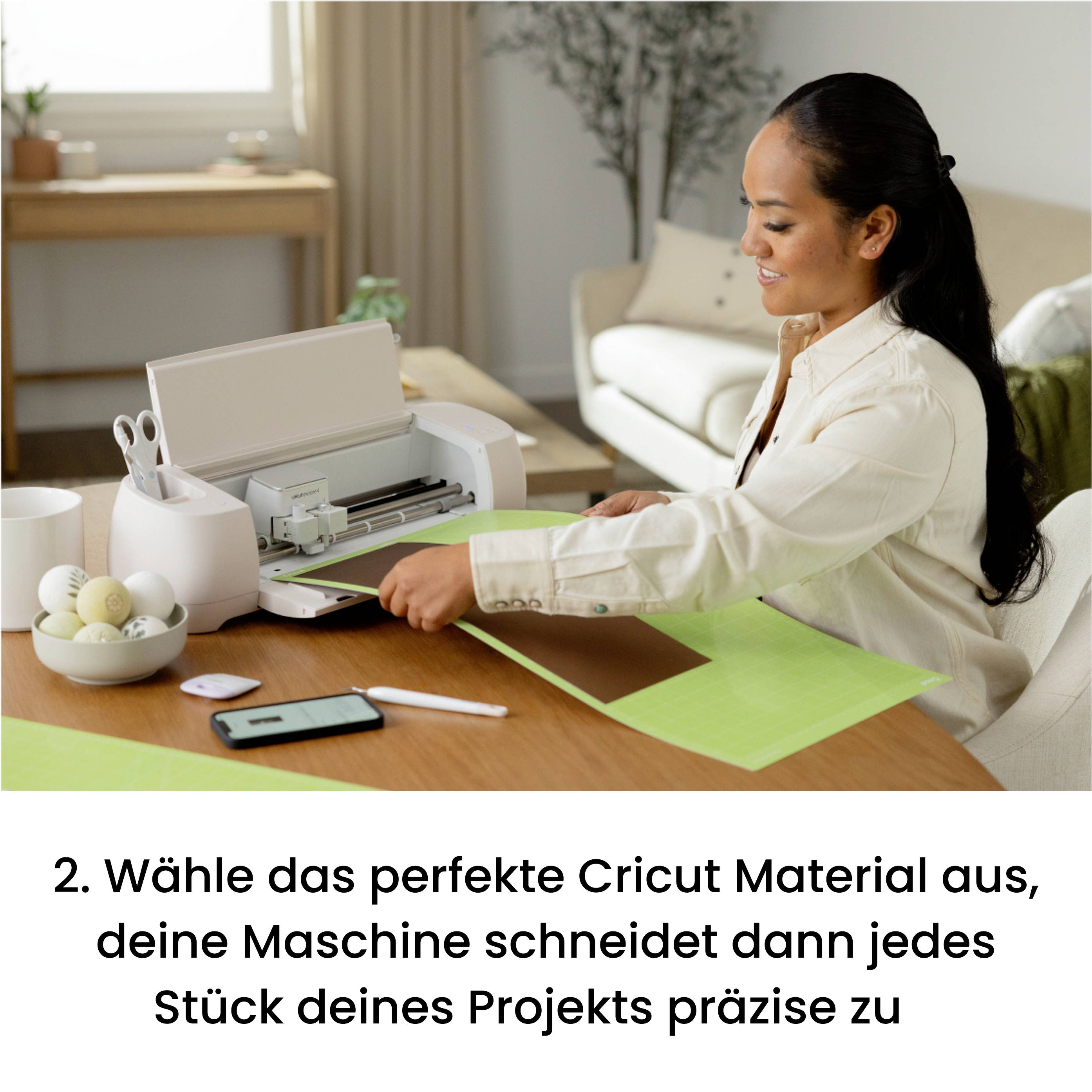 Eine Frau sitzt an einem Tisch mit einem Schneideplotter und bearbeitet ein Bastelprojekt. Im Vordergrund liegen Zubehör und Materialien. Im Hintergrund ist ein Wohnzimmer zu sehen.