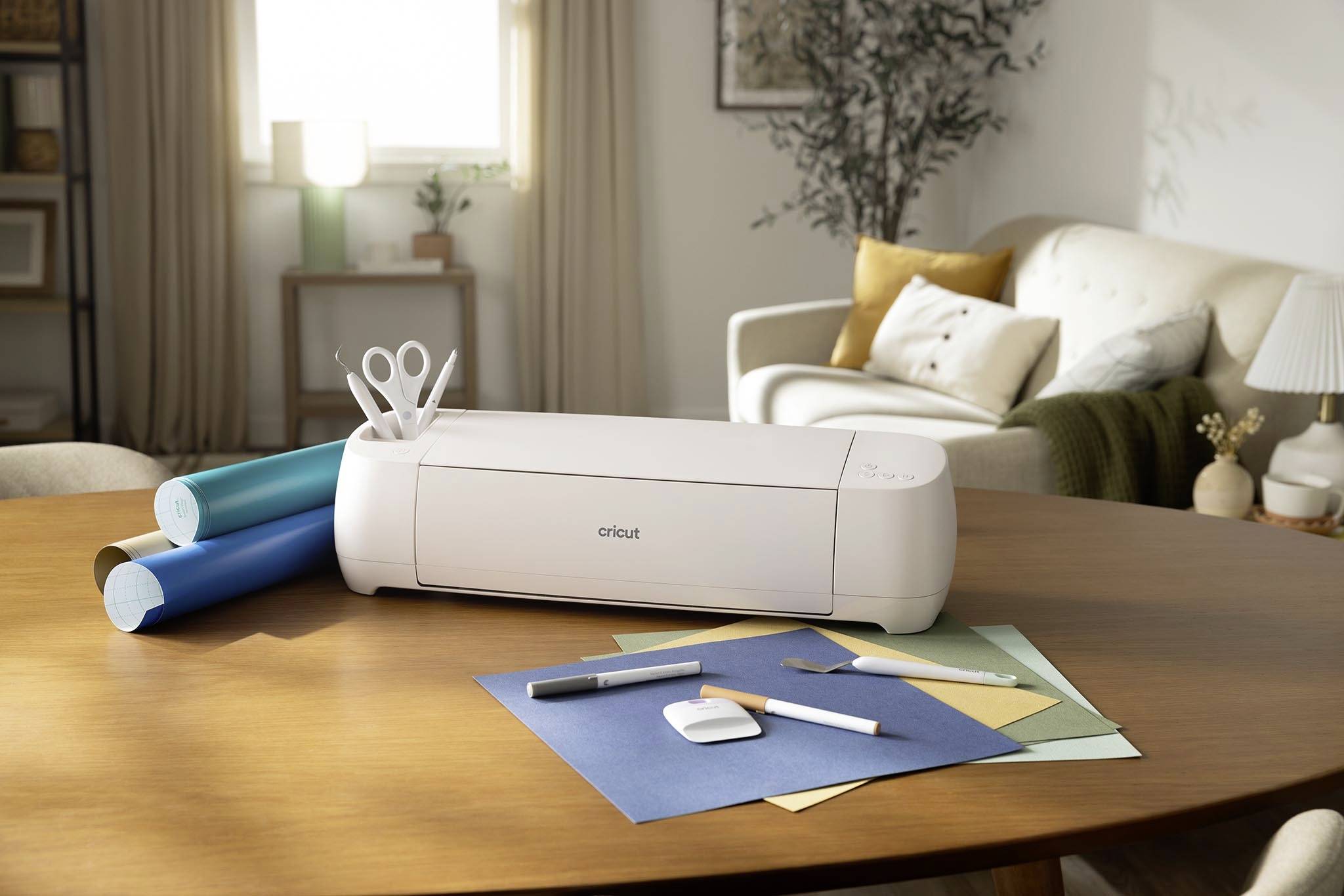 Ein Drucker steht auf einem Tisch, umgeben von farbigem Papier und Handwerkswerkzeugen, in einem gemütlichen Wohnzimmer.