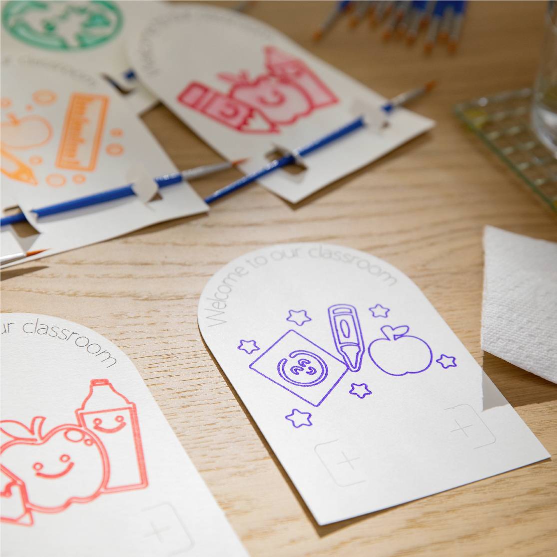 Verschiedene bunte Zeichnungen von Schulzubehör wie Bleistift und Apfel auf Papierblättern auf einem Tisch, im Kunstunterricht.