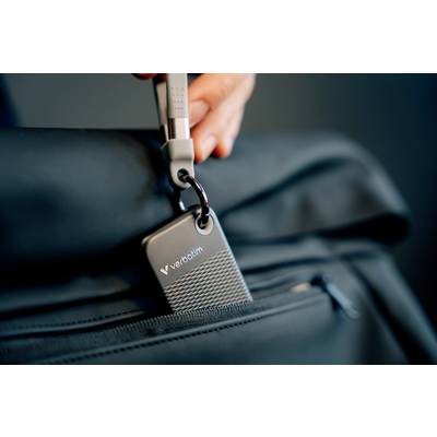 Hand hält einen USB-Stick, der an einem Reißverschluss einer schwarzen Tasche befestigt ist.