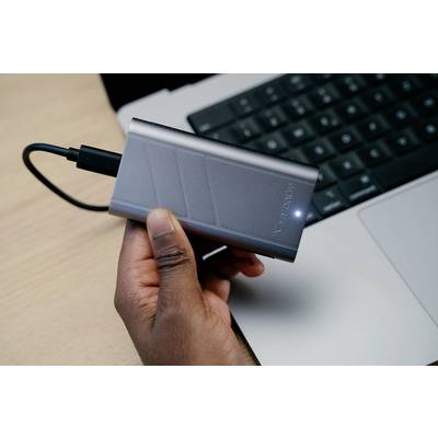 Eine Person hält eine externe Festplatte, die an einen Laptop angeschlossen ist. Die Festplatte hat ein leuchtendes LED-Licht.