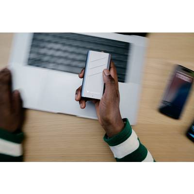 Eine Person hält eine tragbare Festplatte über einem Laptop. Neben dem Laptop liegt ein Smartphone.