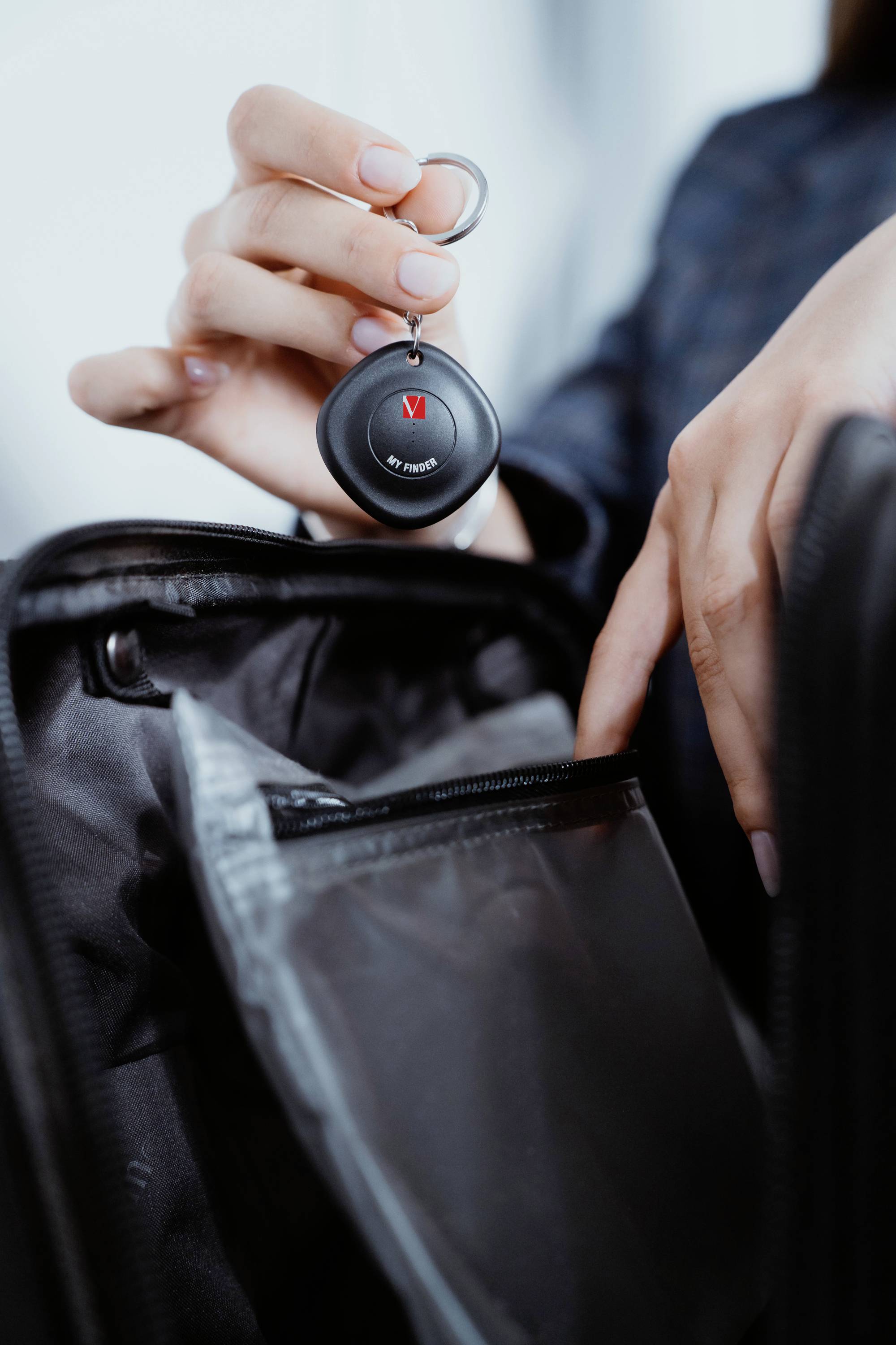 Person hält ein rundes, schwarzes Gerät über einer geöffneten Tasche. Möglicherweise handelt es sich um ein GPS-Tracker-Zubehör.