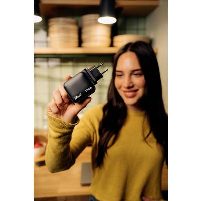 Eine Frau hält ein Ladegerät mit der Aufschrift '100W' in der Hand und lächelt. Im Hintergrund sind Küchelemente sichtbar.