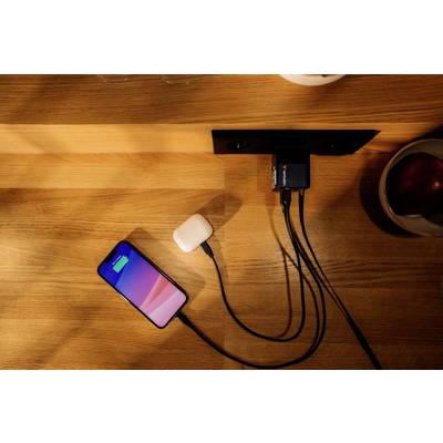 Ein Smartphone und drahtlose Kopfhörer werden auf einem Holztisch gleichzeitig über ein Ladegerät an der Wand aufgeladen.