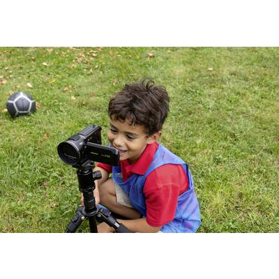 Ein Junge sitzt auf einer Wiese und filmt mit einer Videokamera auf einem Stativ. Ein Fußball liegt im Hintergrund auf dem Gras.