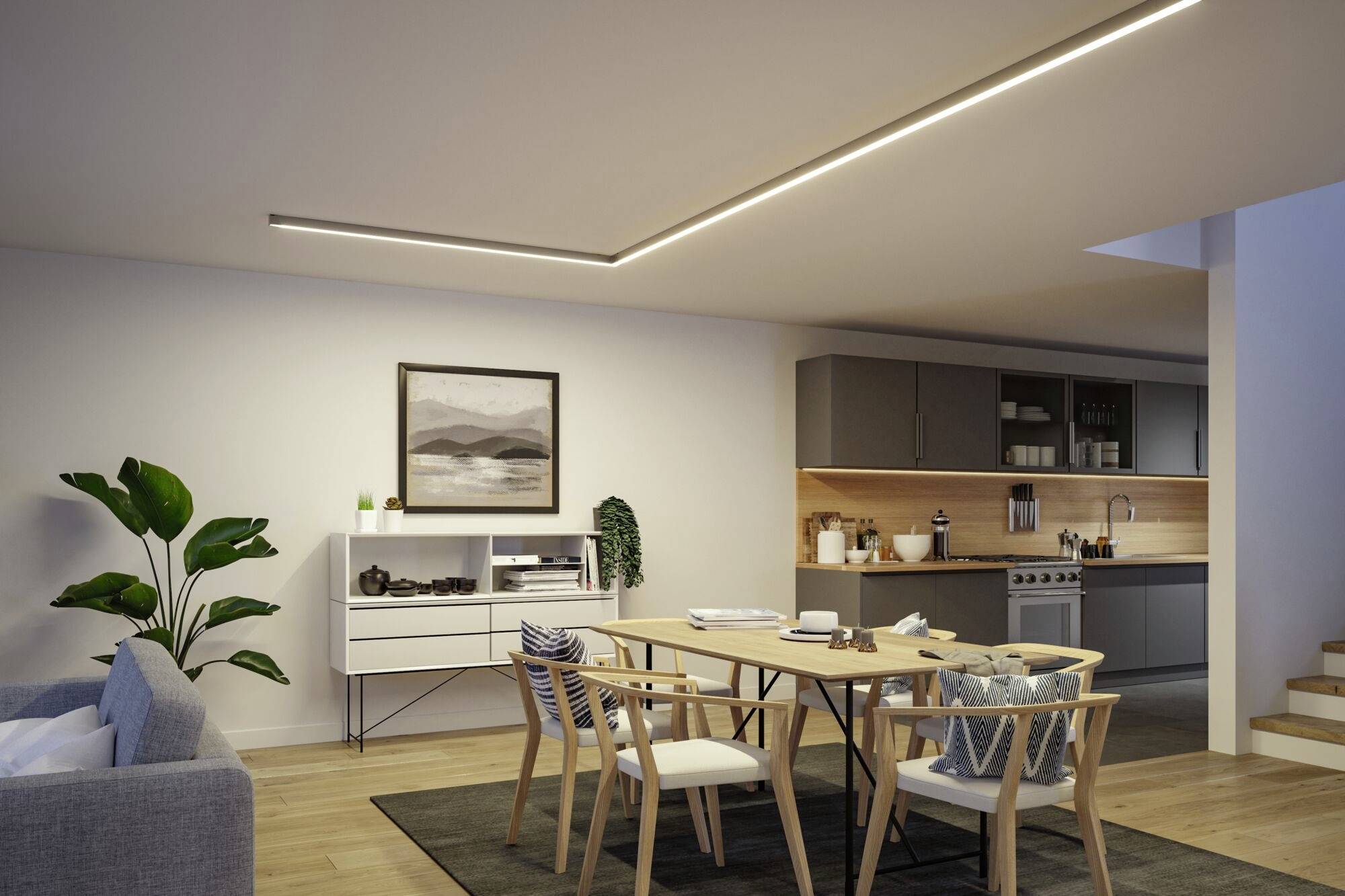 Der Raum zeigt ein modernes Wohnzimmer mit offener Küche. Essbereich mit Holztisch und Stühlen, graues Sofa, Pflanzen, Kunst an der Wand.