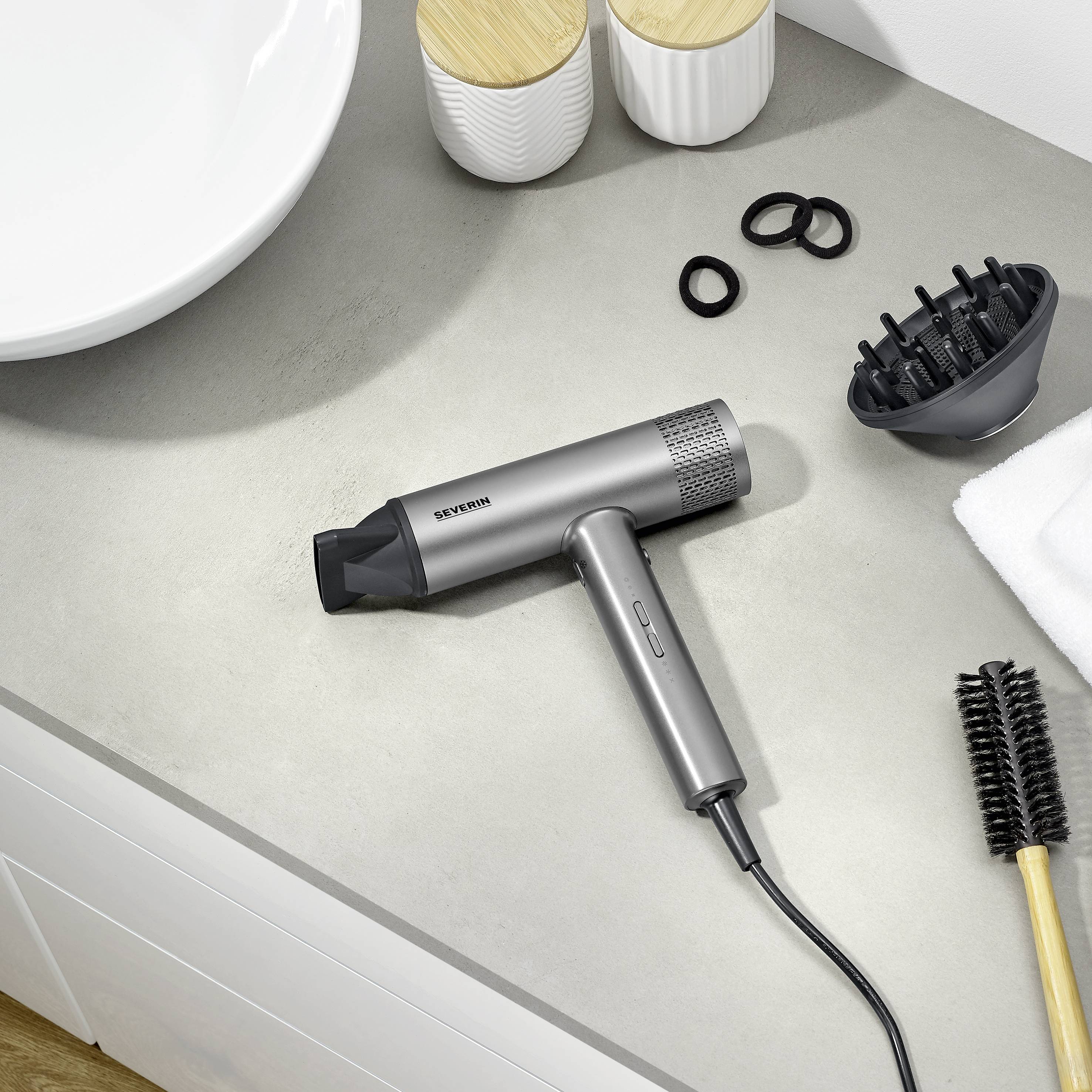 Ein Föhn auf einer Badezimmerablage neben einem Kamm und Haargummis. Die Szene zeigt typische Haarstyling-Werkzeuge.