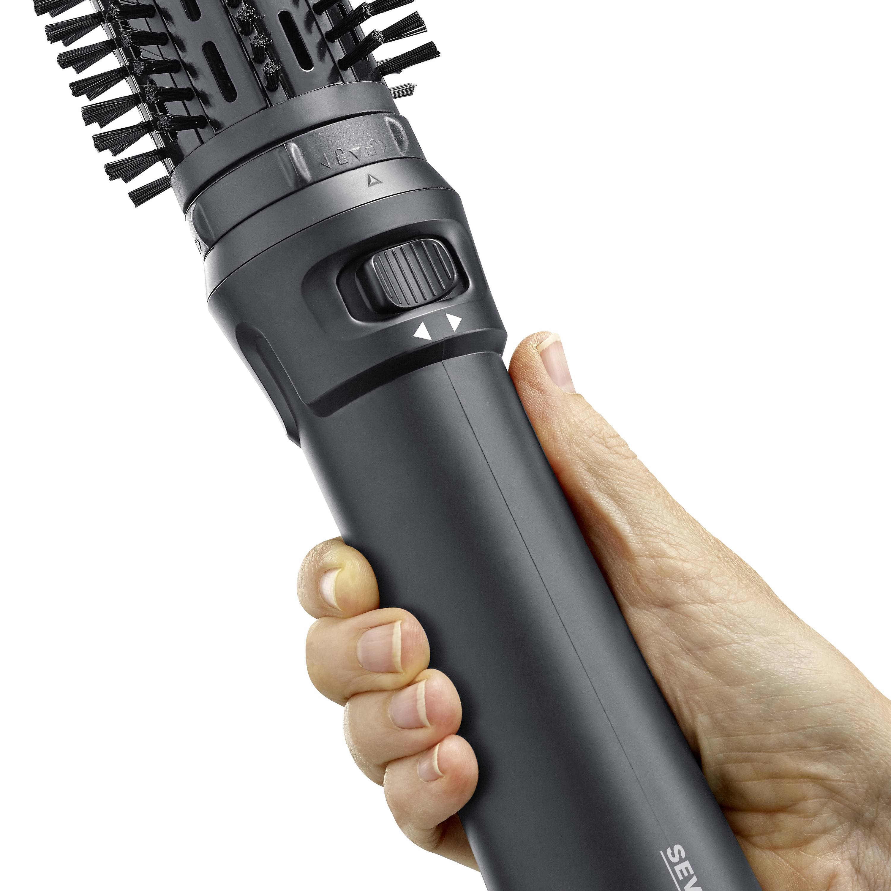 Eine Hand hält eine schwarze Haarbürste mit integriertem Haartrockner. 