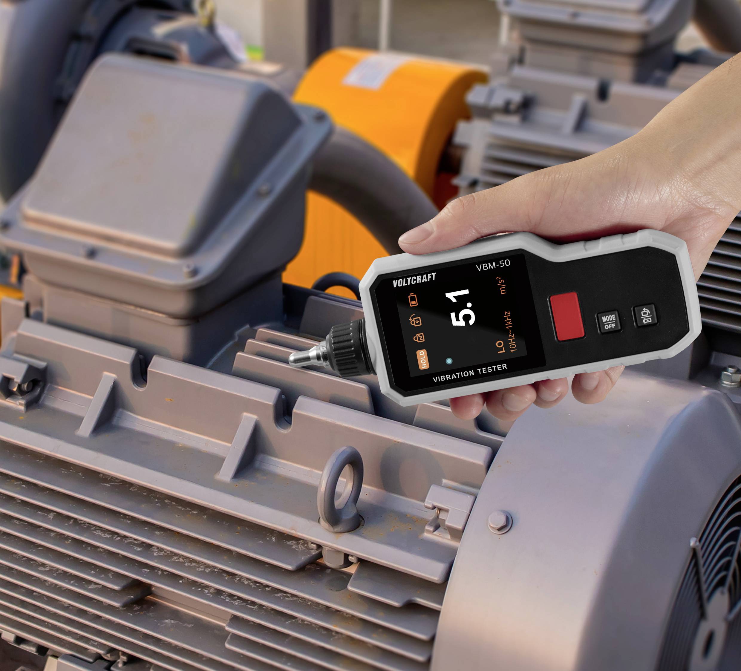 Eine Person verwendet einen tragbaren Vibrationsprüfer an industrieller Maschinerie und zeigt eine Messung von '5,1' an.