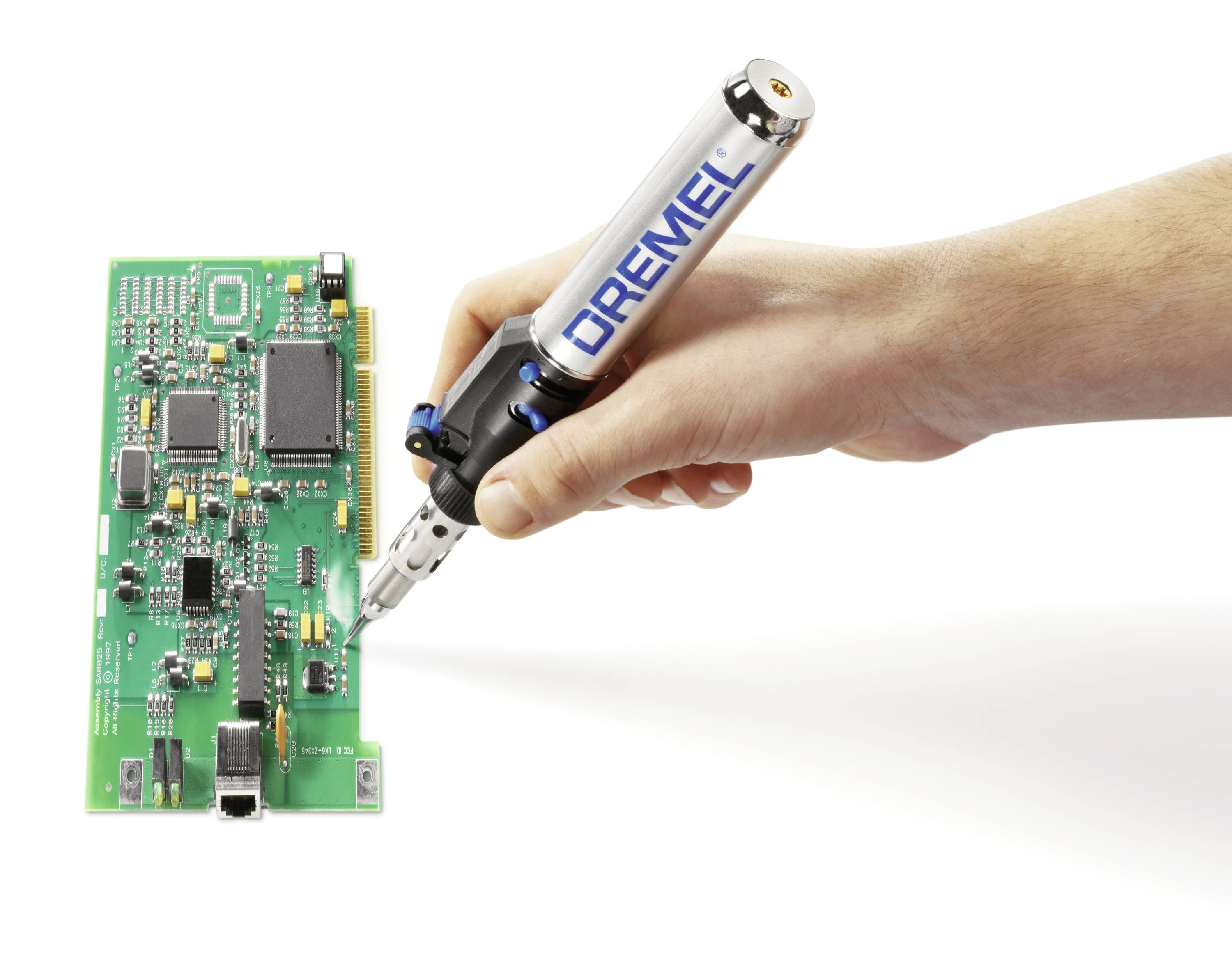 'Nahaufnahme einer Hand, die mit einem Dremel-Werkzeug an einer grünen Leiterplatte arbeitet, auf der verschiedene elektronische Komponenten sind.'