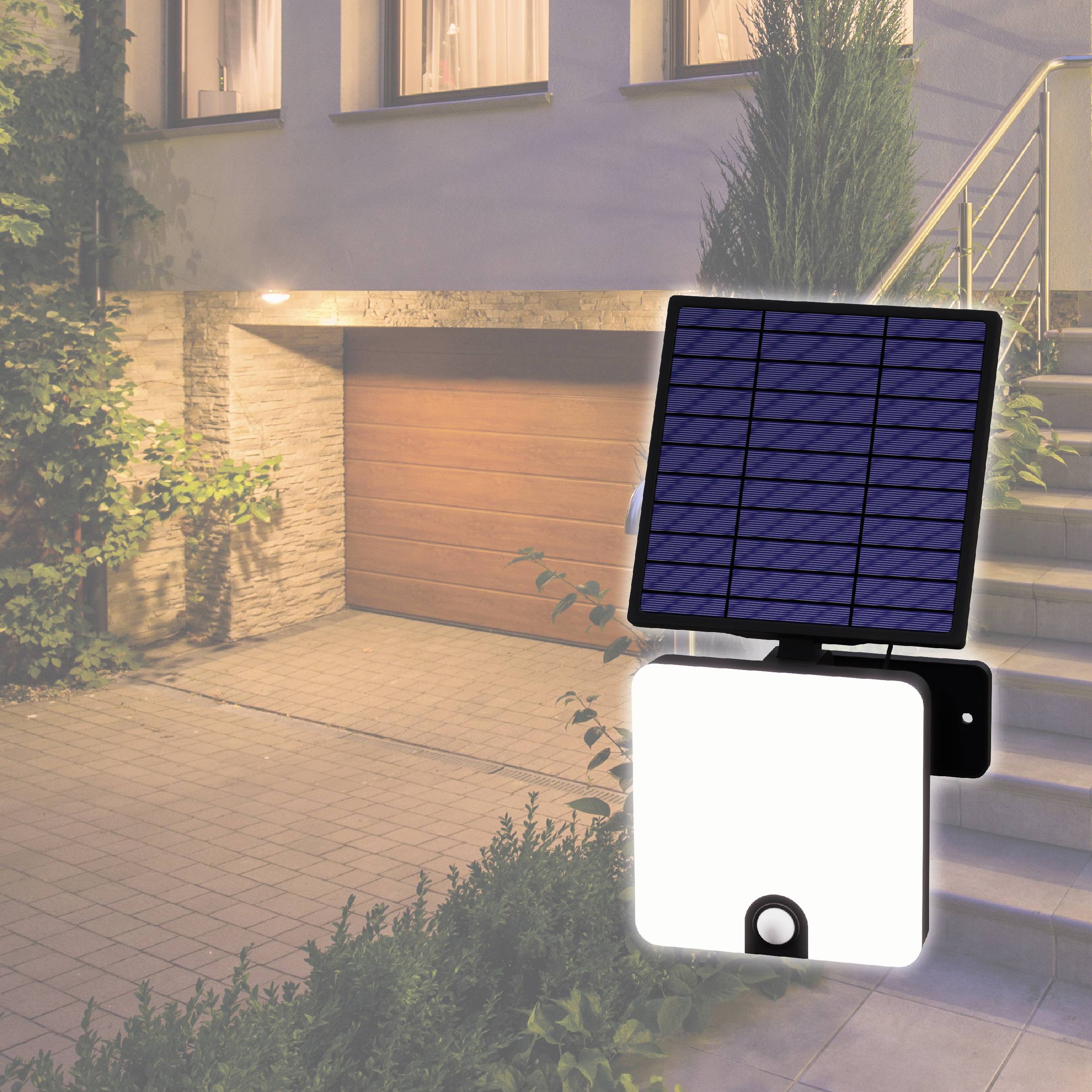 Ein Solarmodul mit angehängtem Licht ist an einer Hausfassade neben einer Garage angebracht. Ein Teil des Gartens ist sichtbar.
