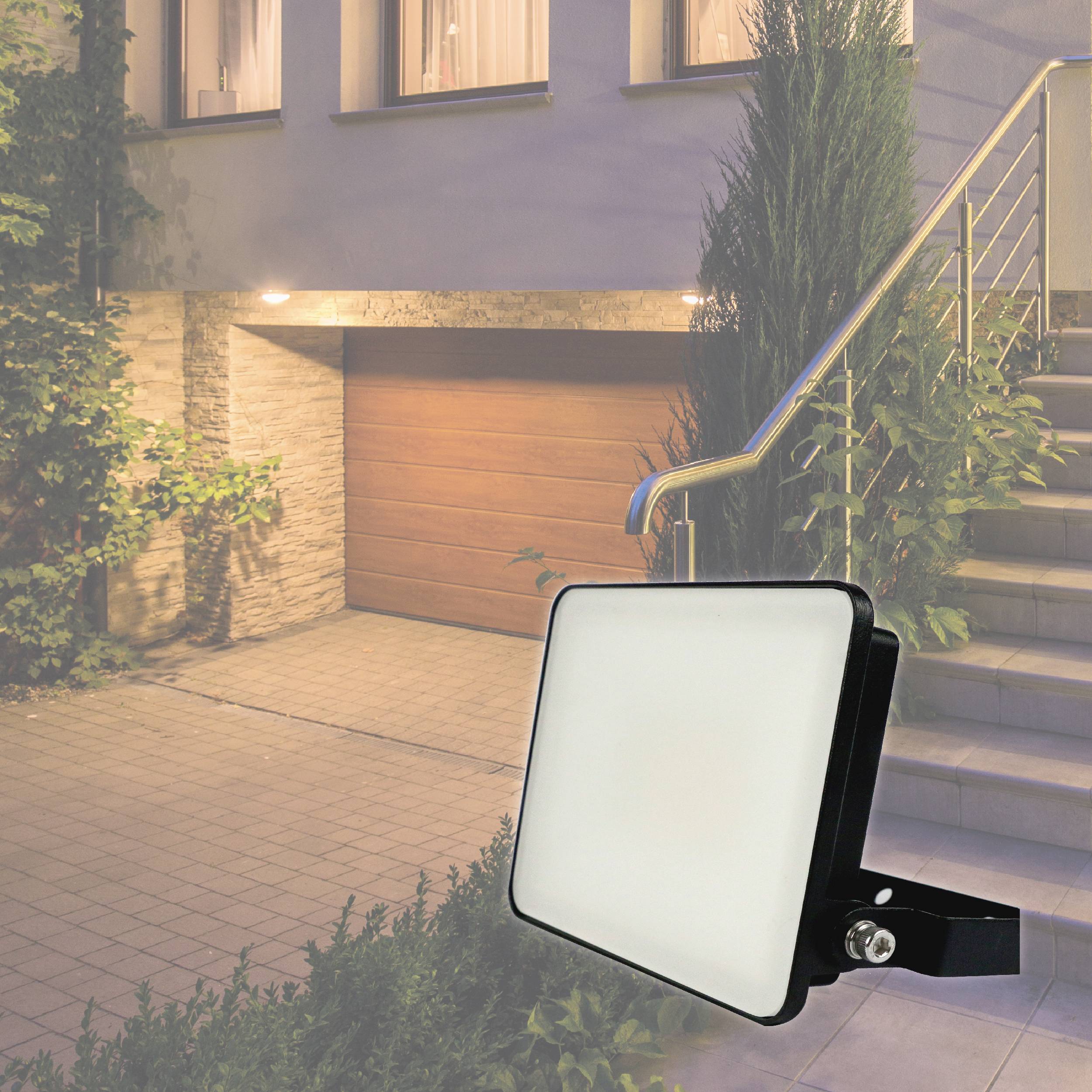Ein heller LED-Strahler leuchtet eine Garage mit bepflanztem Weg darunter aus.