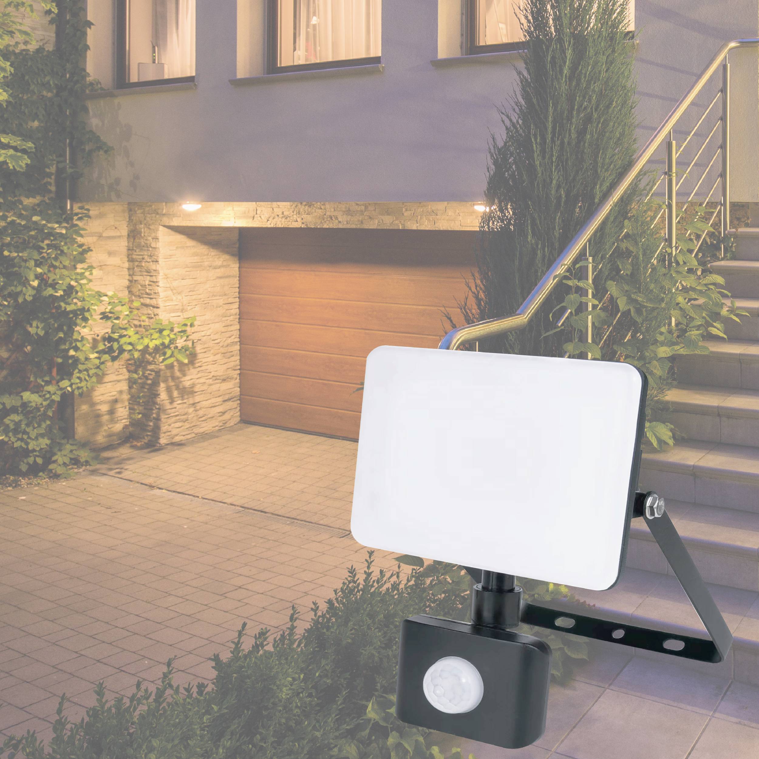 Außenlampe mit integriertem Bewegungsmelder beleuchtet gepflasterten Hof mit angrenzender Treppe und Pflanzenecke.