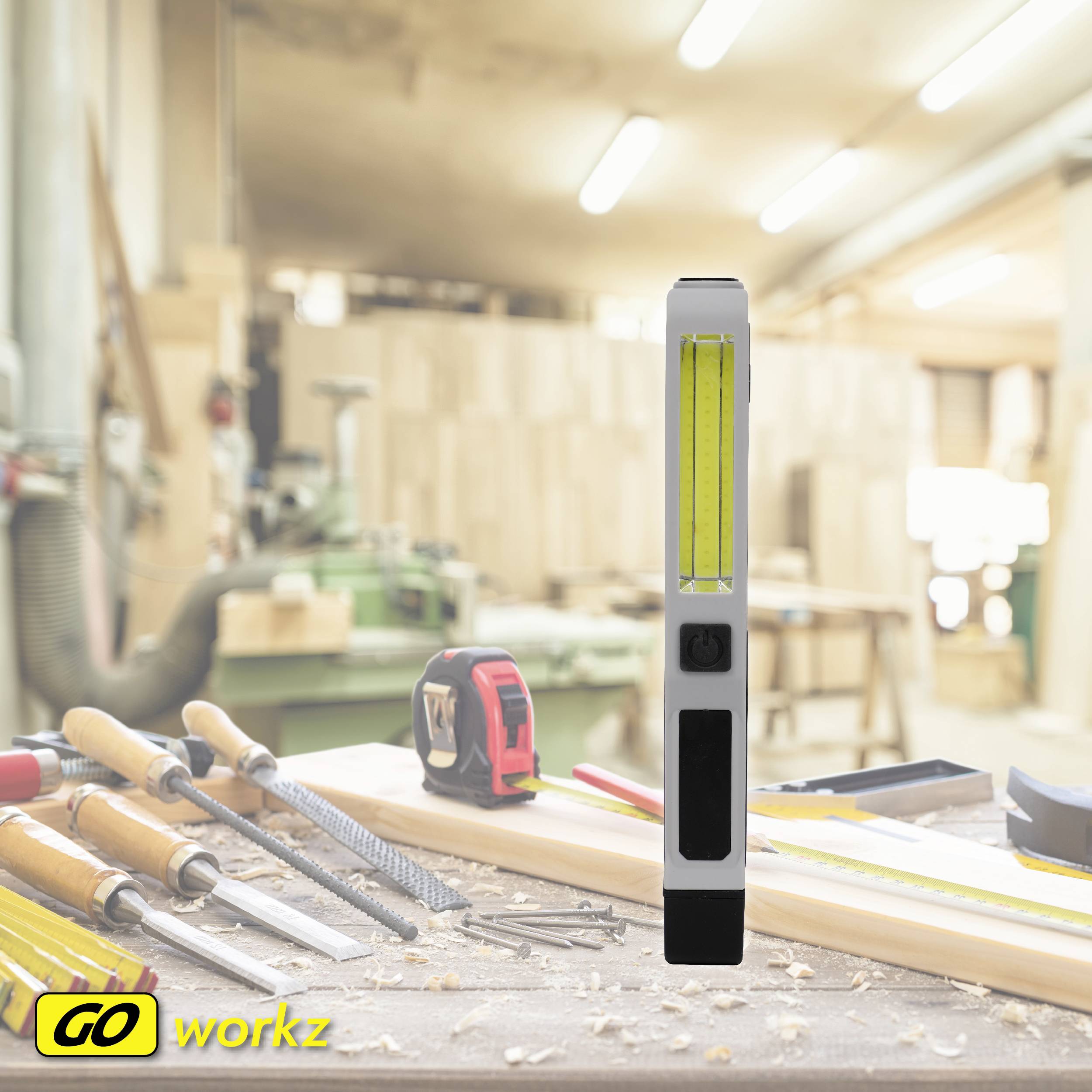 Zu sehen ist eine Werkbank in einer Tischlerei mit verschiedenen Werkzeugen wie Feilen und Maßband. Im Hintergrund sind Holzmaschinen.