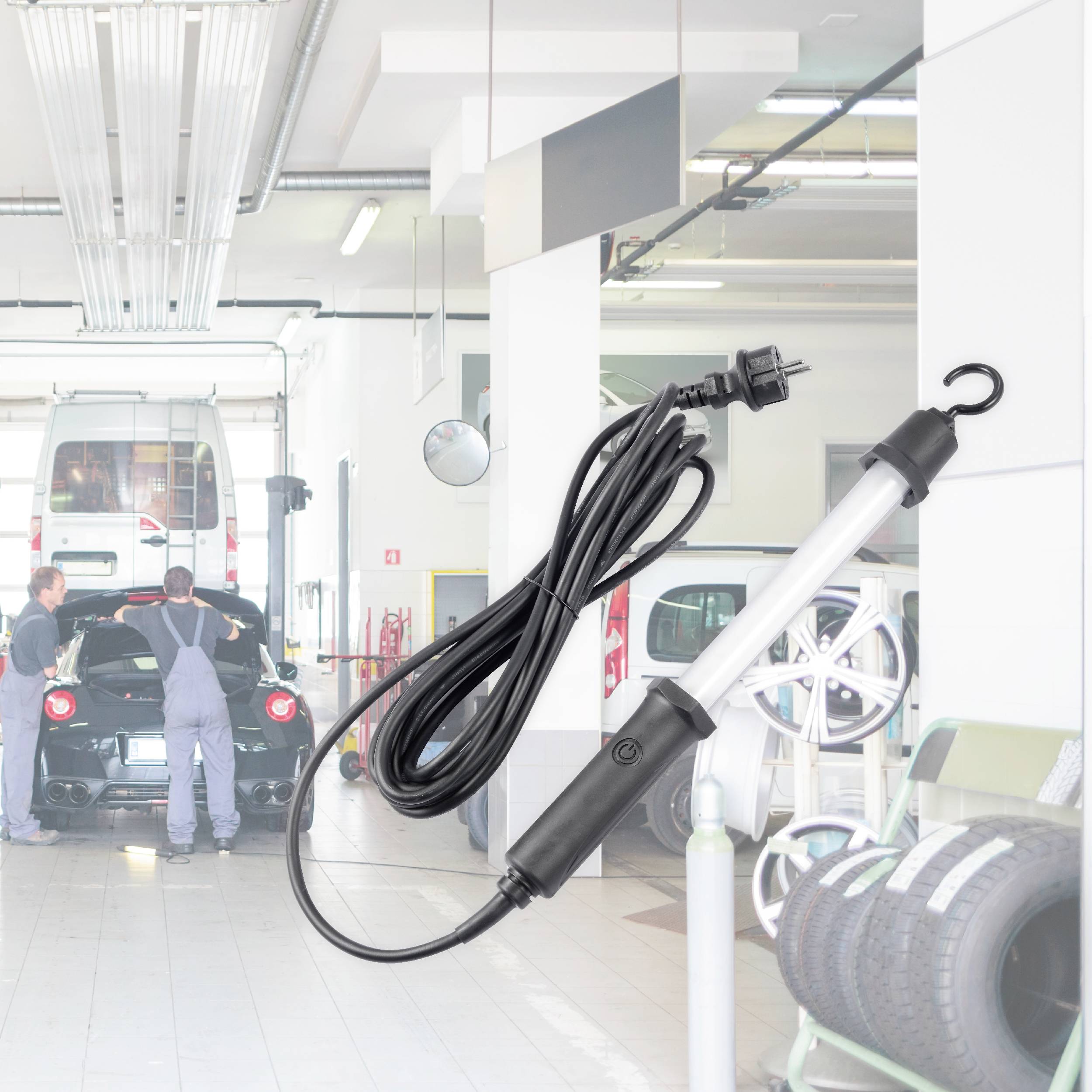 Autowerkstatt mit zwei Mechanikern, die an einem Sportwagen arbeiten. Im Vordergrund eine Werkstattlampe mit langem Kabel.