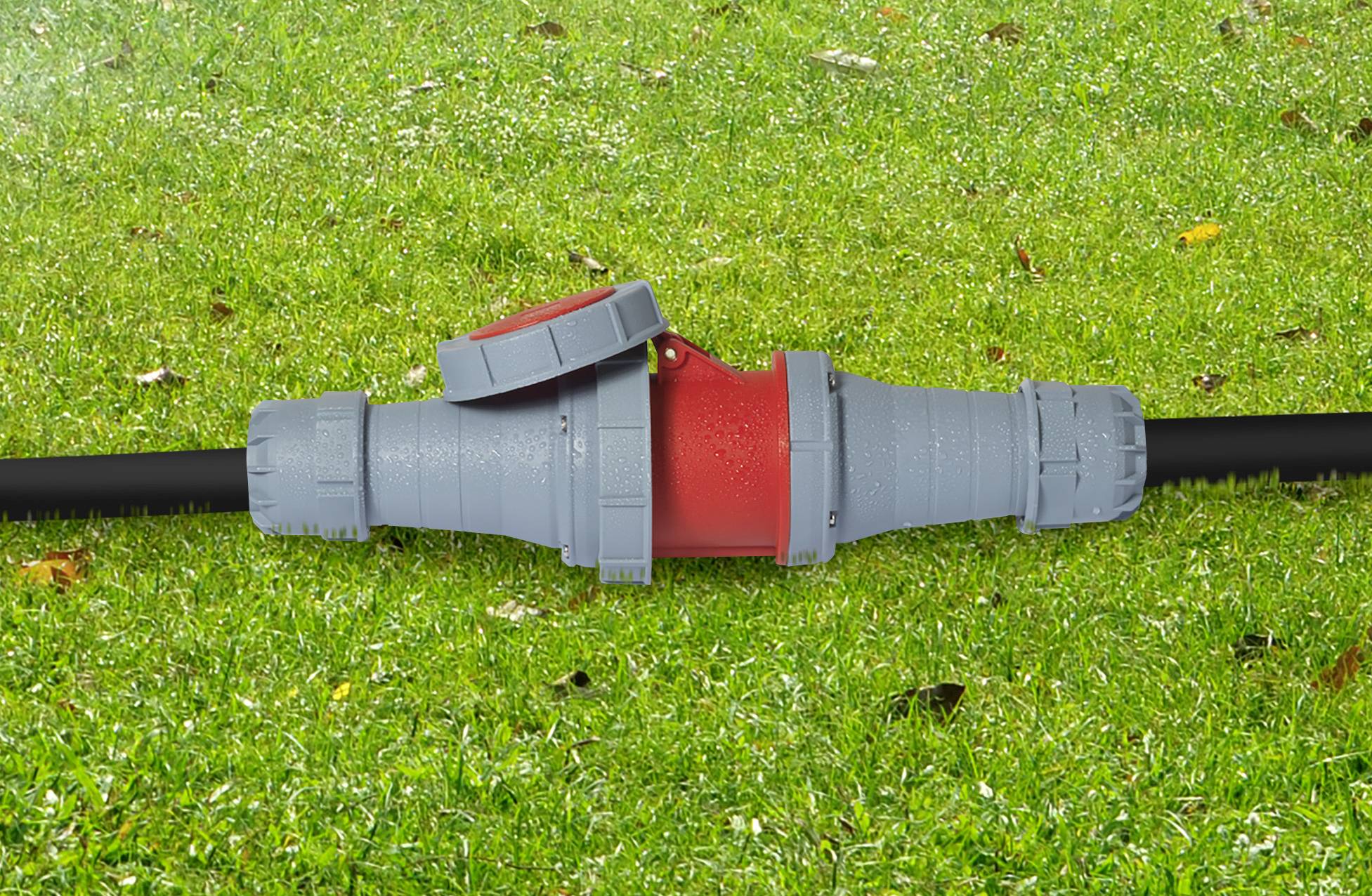 Ein graues Rohrstück mit einem roten Mittelteil und einem offenen Deckel liegt auf grünem Rasen.