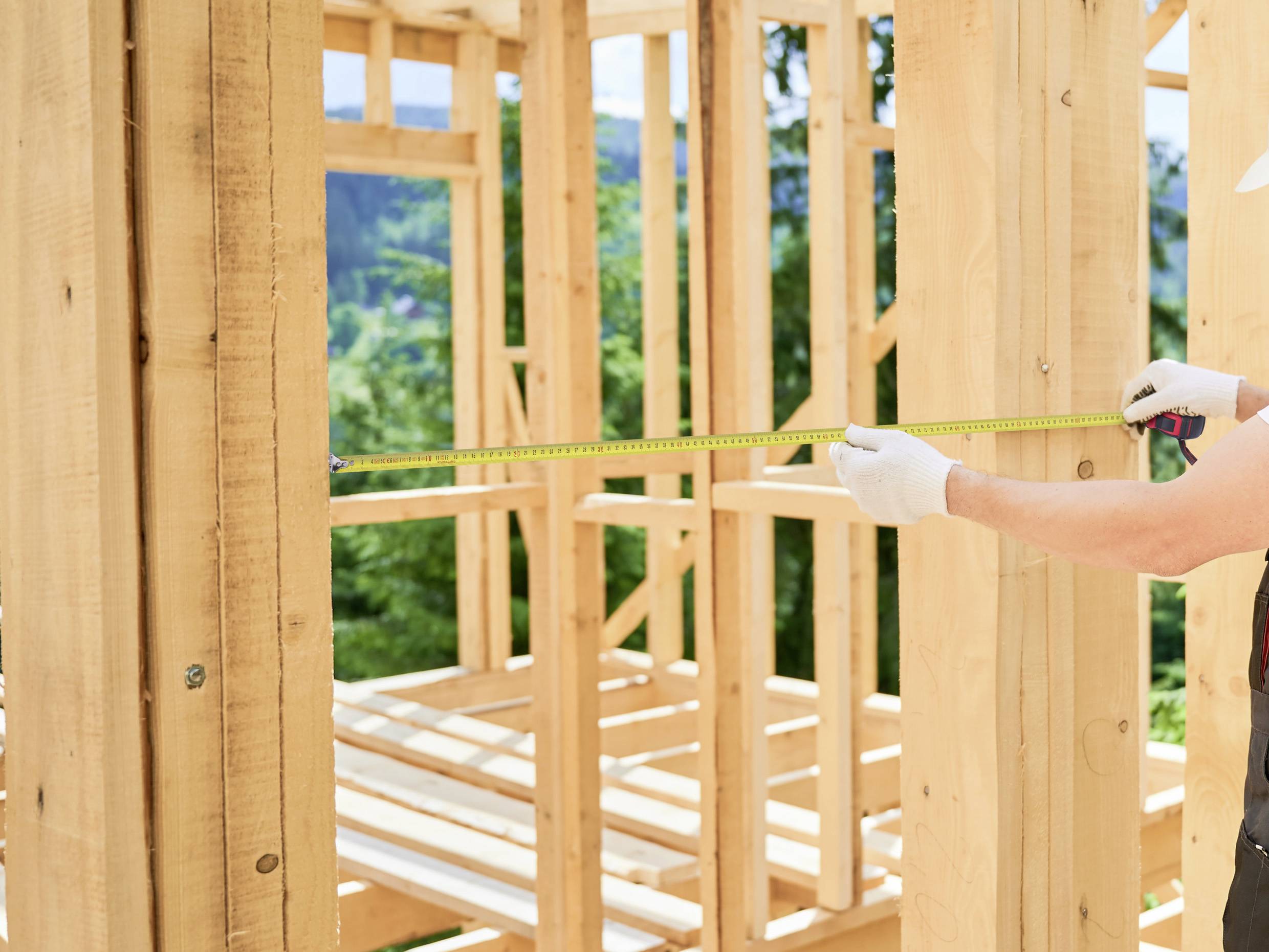 Person, die einen Holzrahmen mit einem Maßband vermisst, im Freien.