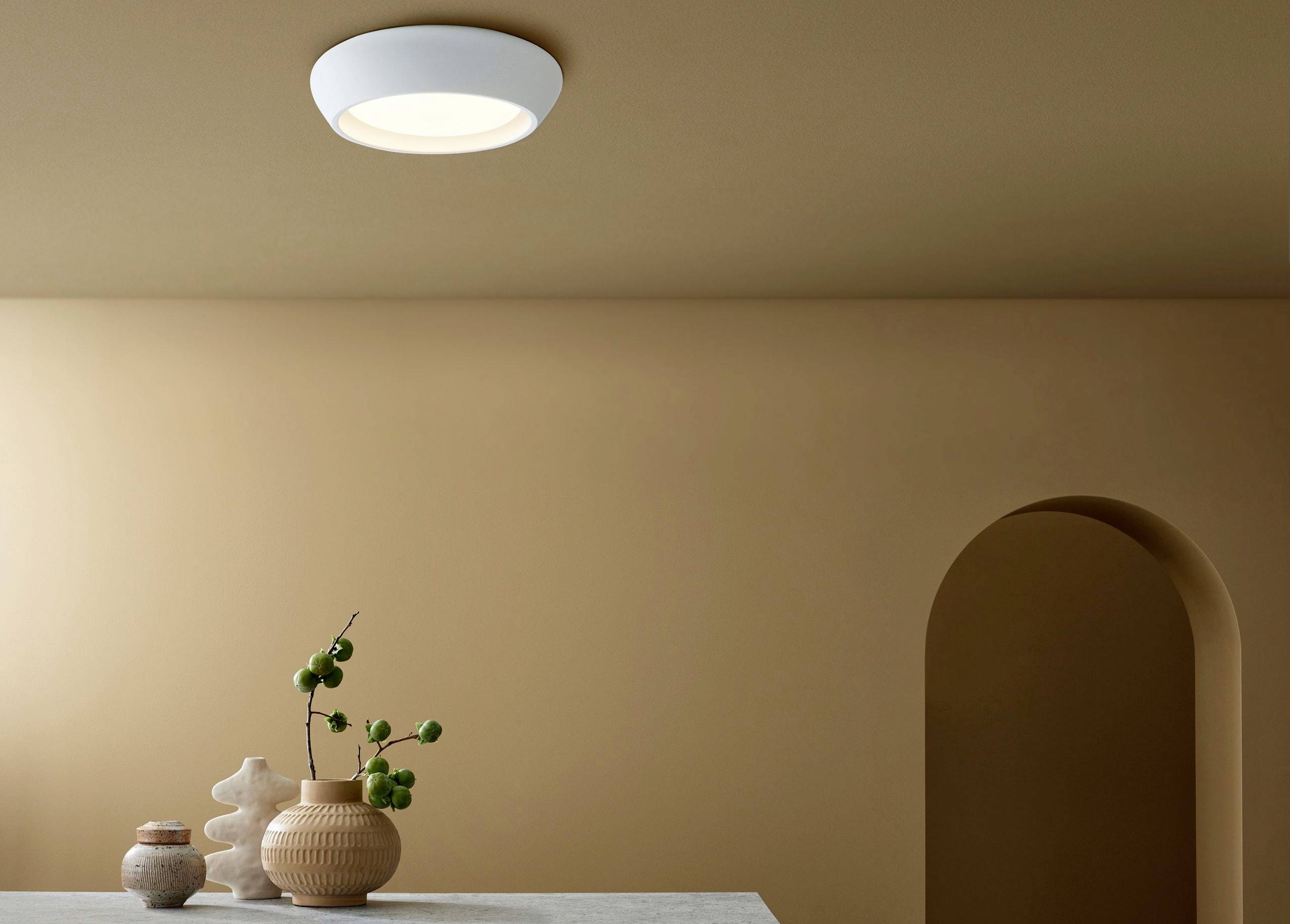 Deckenlampe leuchtet in minimalistisch eingerichteten Raum mit beigen Wänden und dekorativer Vase auf Tisch.
