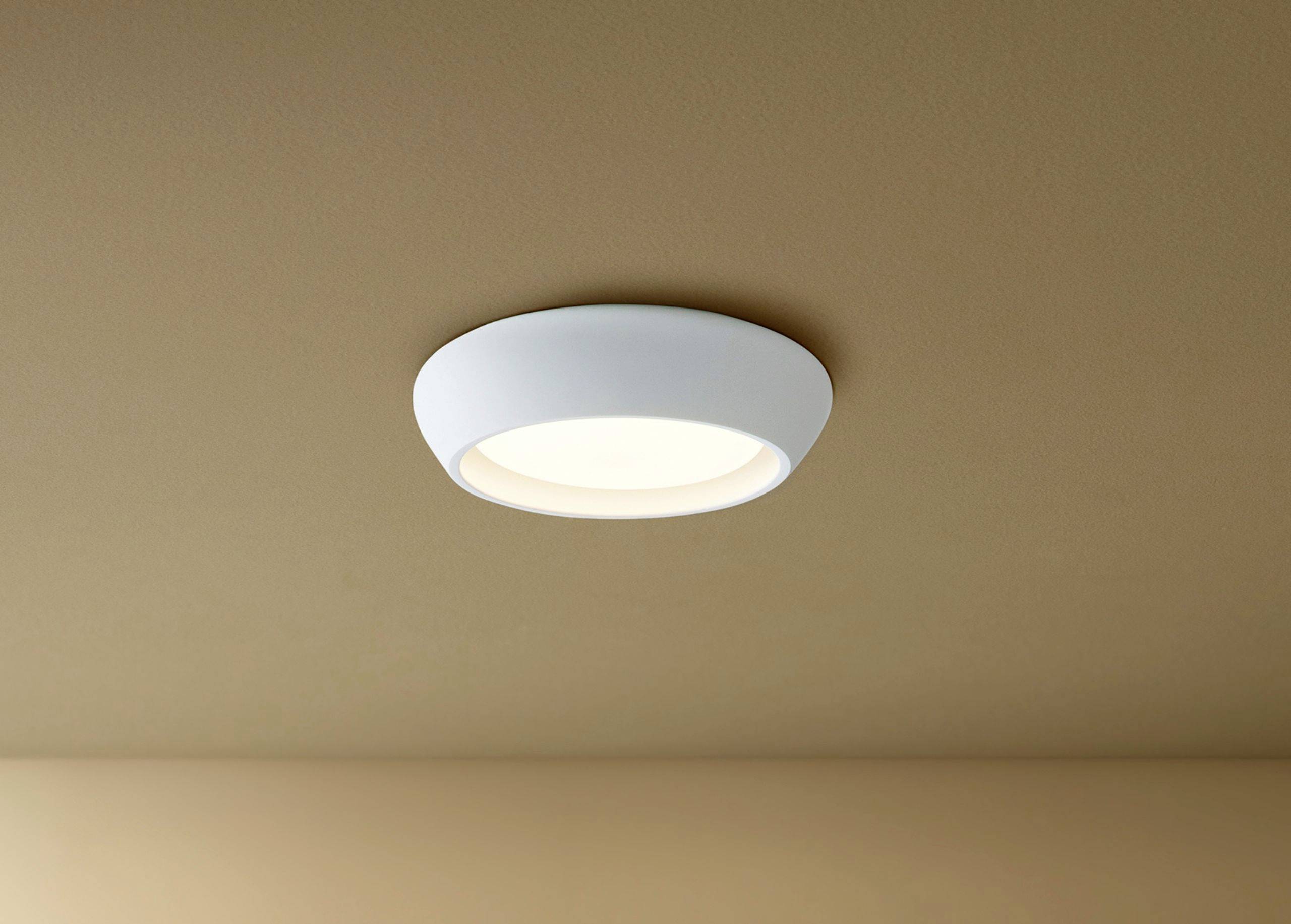 Eine runde LED-Deckenleuchte mit weißem Rahmen, montiert an einer beigen Zimmerdecke, strahlt warmes Licht aus.