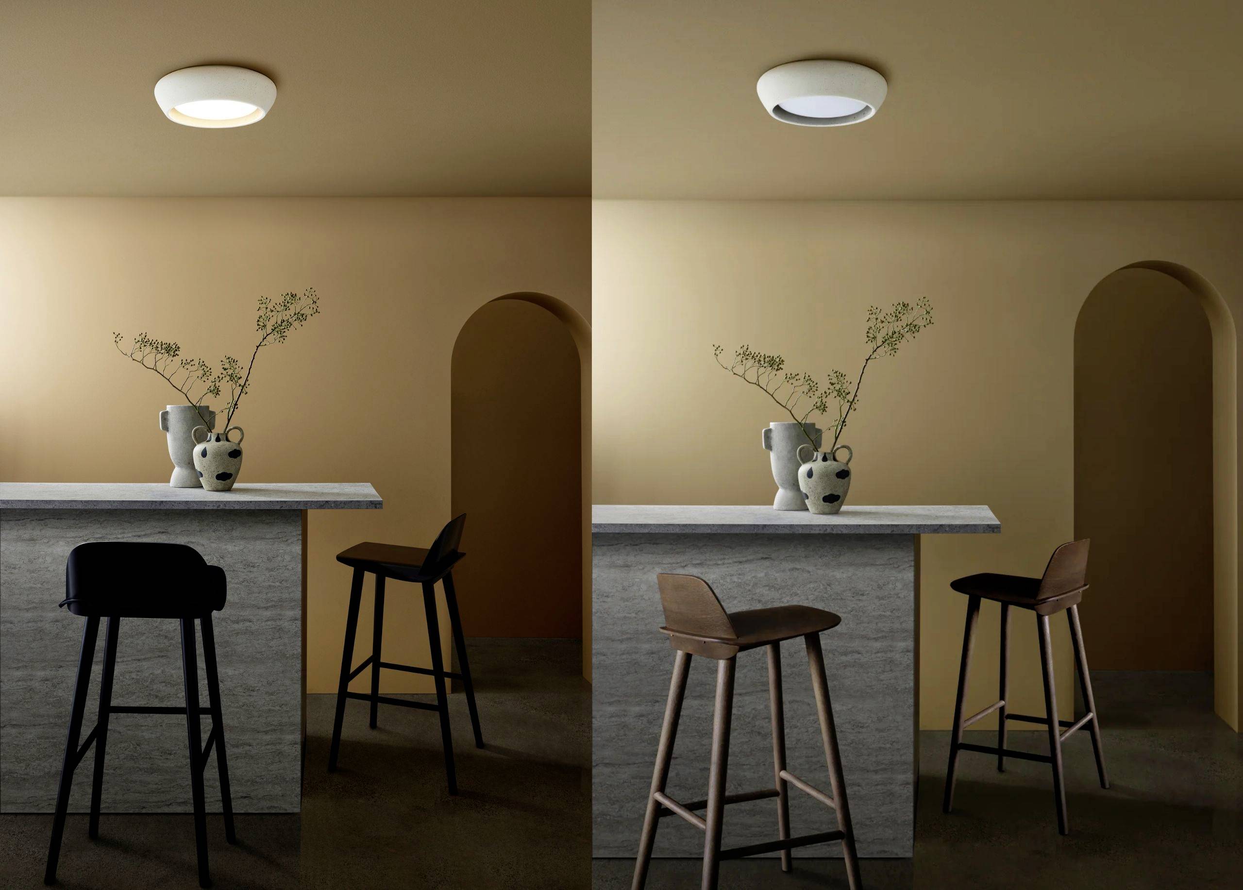 Zwei moderne Stehlampen in einem Raum mit minimalistischer Einrichtung; Vase mit Zweigen auf Marmortresen, Hocker davor.