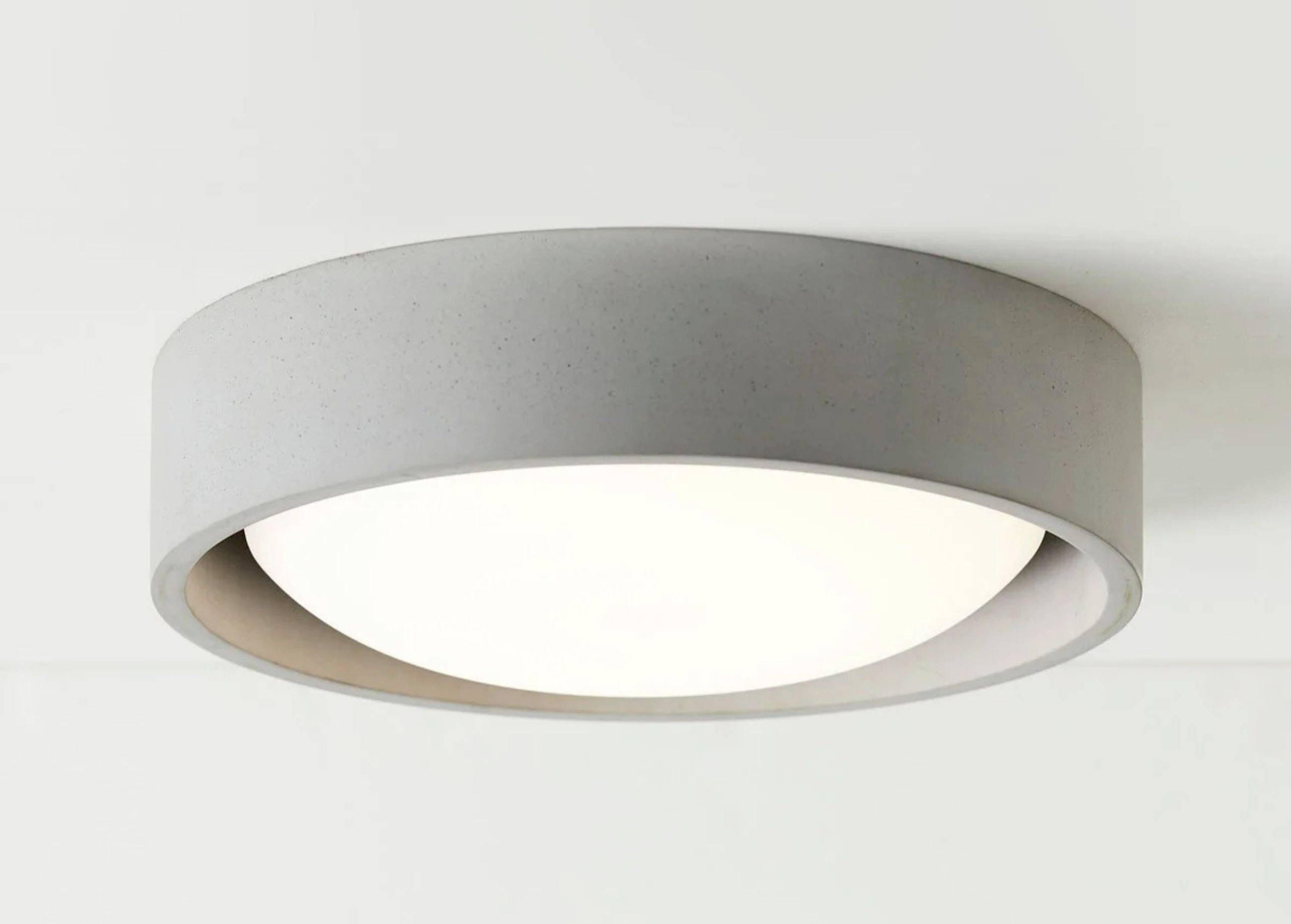 Graue Deckenleuchte mit rundem, minimalistischem Design und weicher, gleichmäßiger Lichtverteilung, an einer weißen Decke montiert.