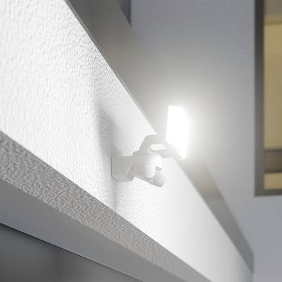 Ein heller Bewegungsmelder strahlt an der Wand eines Hauses, umgeben von Dämmerung. Tür im Hintergrund angedeutet.