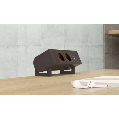 Eine schwarze Tischsteckdosenleiste mit zwei Steckdosen ist auf einem Holztisch montiert. Neben der Leiste liegen zwei zusammengelegte Papierrollen.