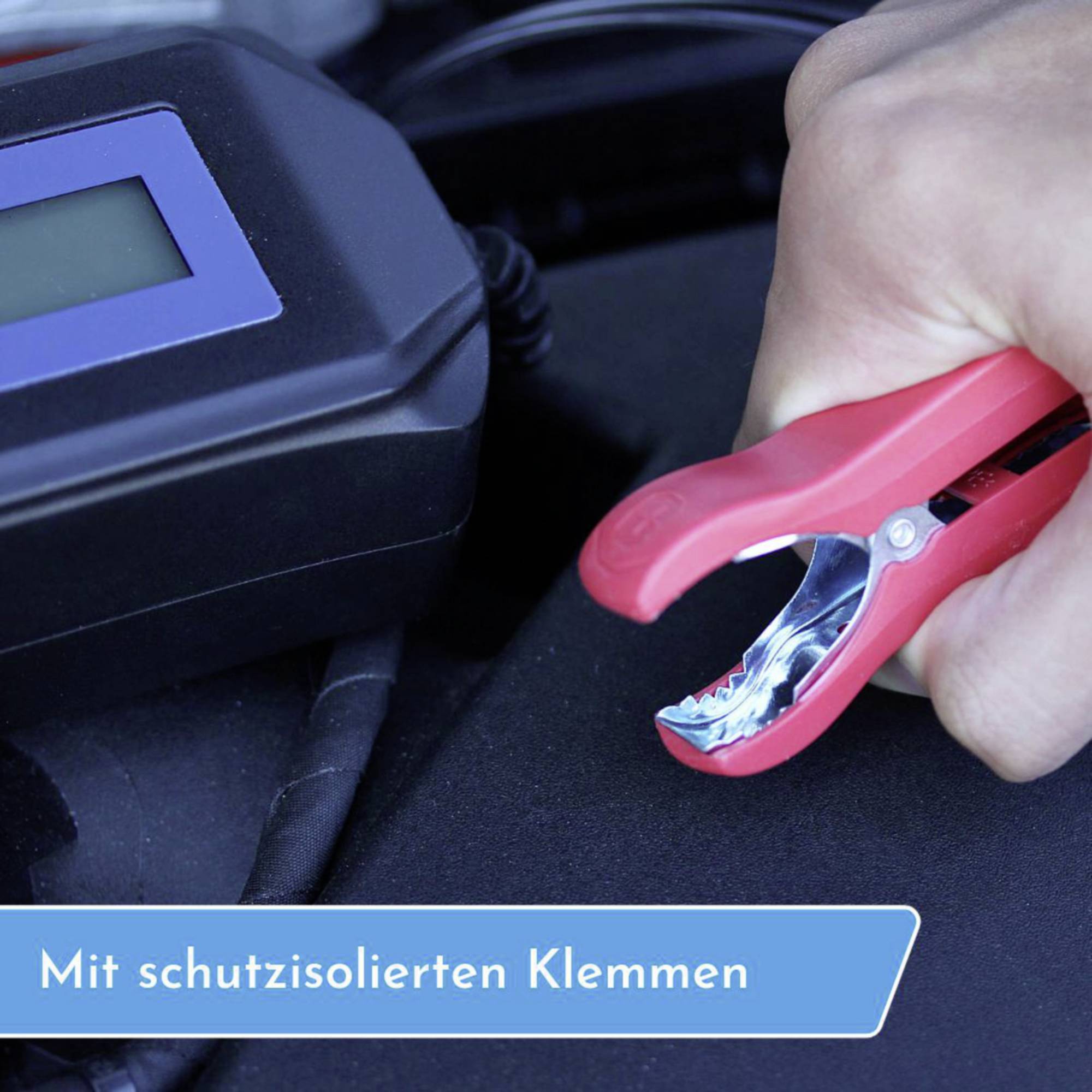 Eine Hand hält eine rote Krokodilklemme mit Schutzisolierung. Ein blaues Display ist im Hintergrund zu sehen. Text: 'Mit schutzisolierten Klemmen'.