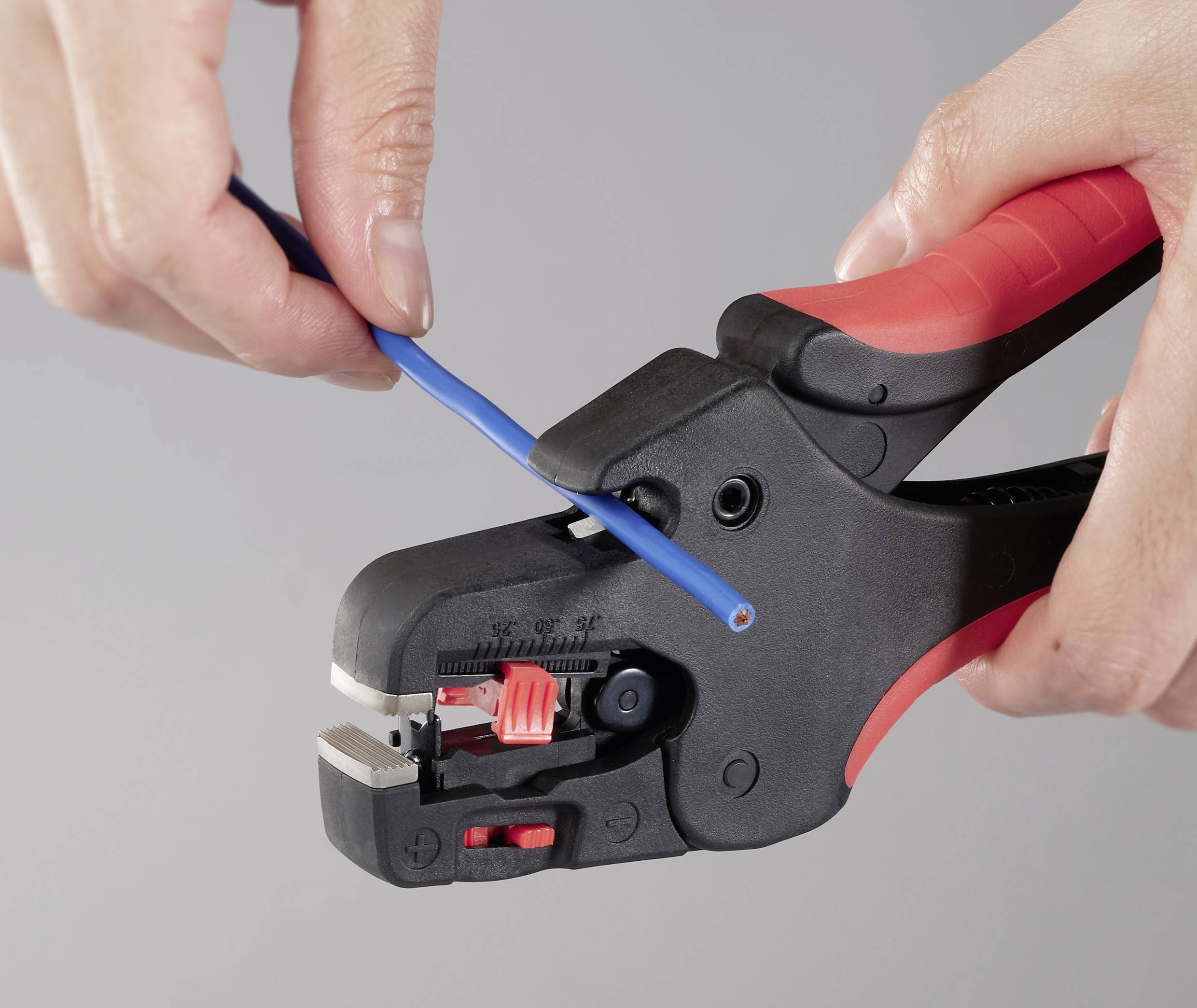 Eine Nahaufnahme von Händen, die ein Abisolierwerkzeug verwenden, um die Isolation von einem blauen Kabel zu entfernen, wobei eine präzise Grifftechnik und Werkzeughandhabung gezeigt wird.