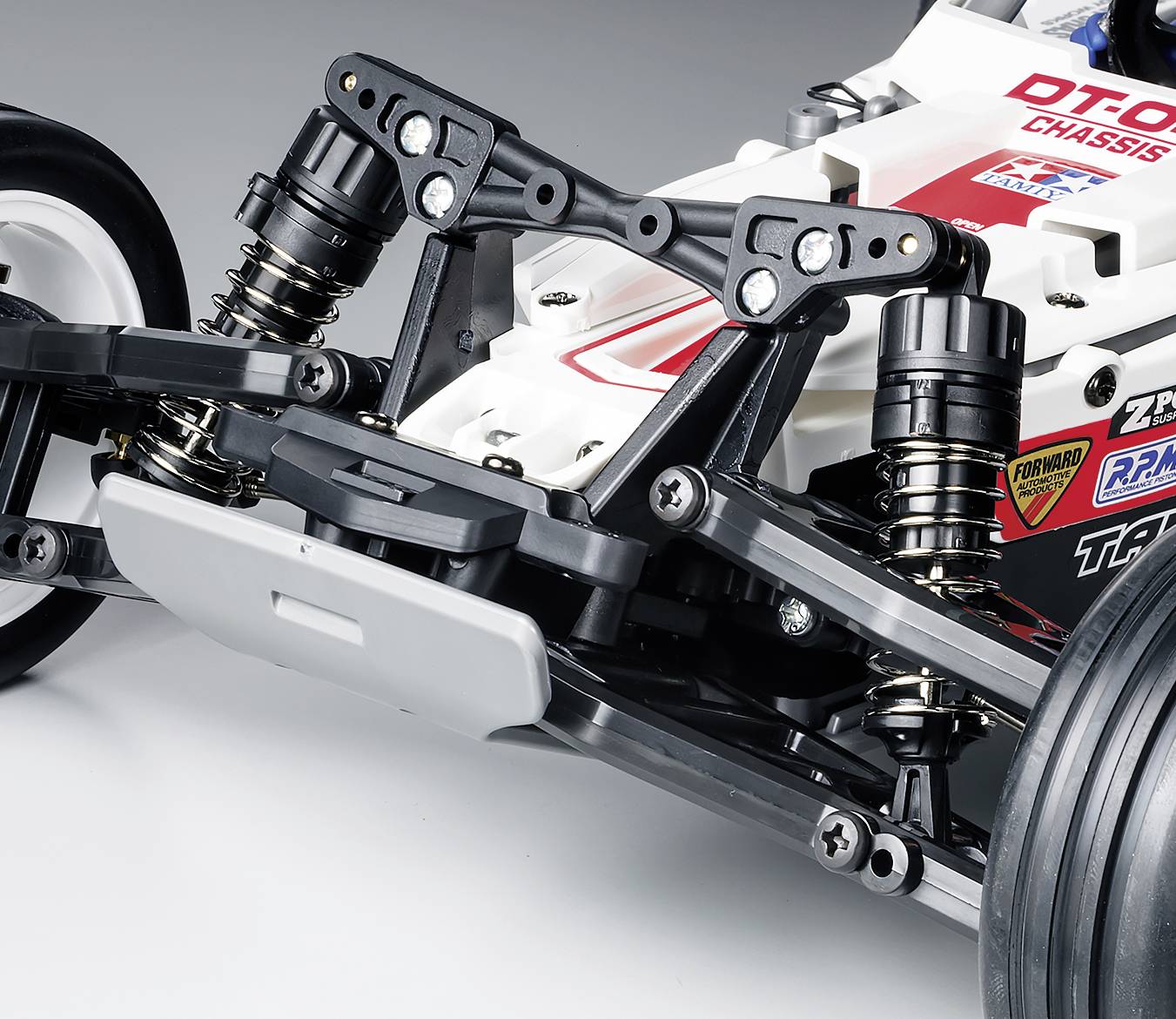 Nahaufnahme des vorderen Aufhängungssystems eines Modellautos mit Stoßdämpfern und Reifen, zeigt technische Details und Aufkleber.