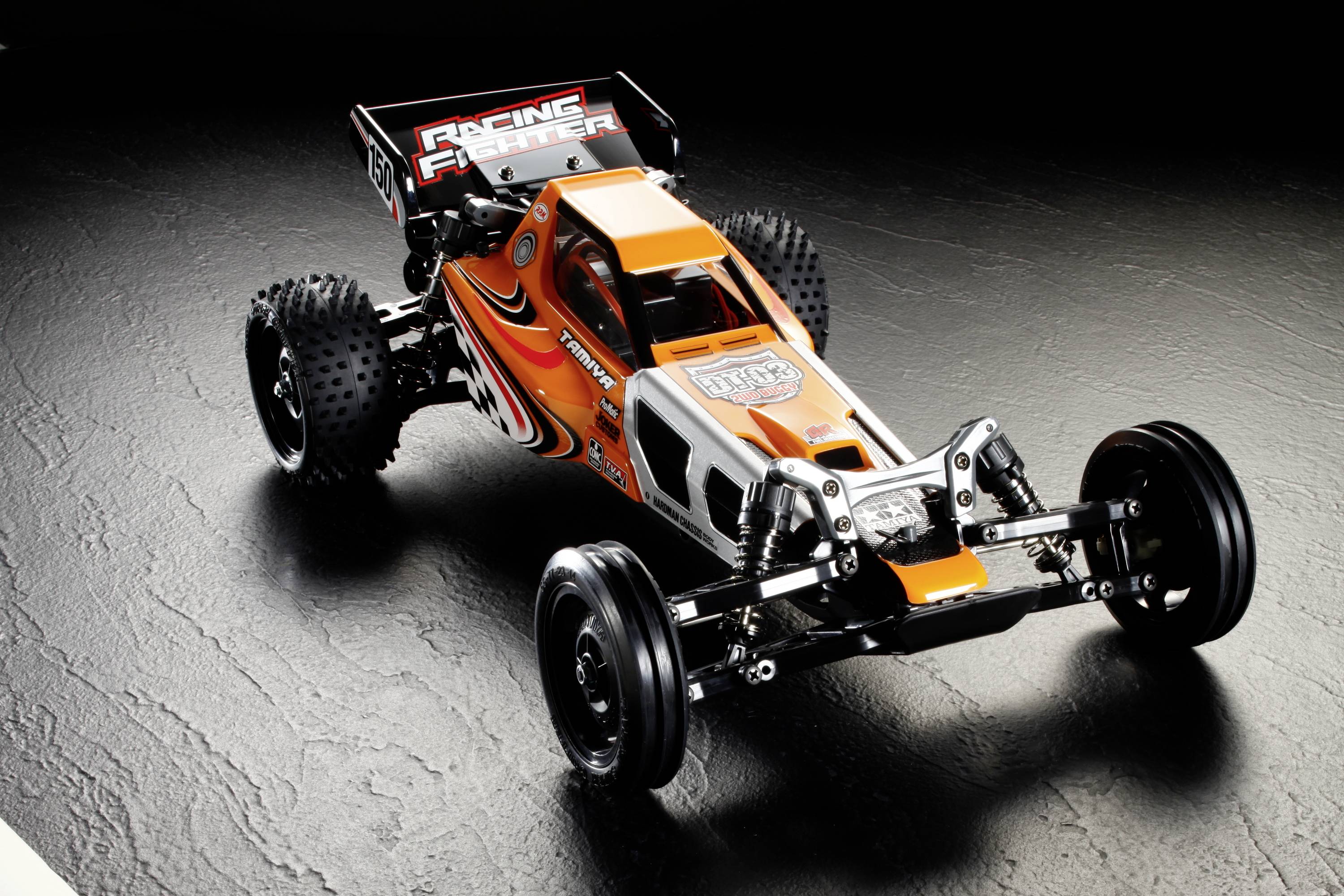 RC-Auto mit orange-schwarzem Design auf schwarzem Untergrund. Grobe Reifen und Schriftzug 'Racing Fighter' am Heckflügel.