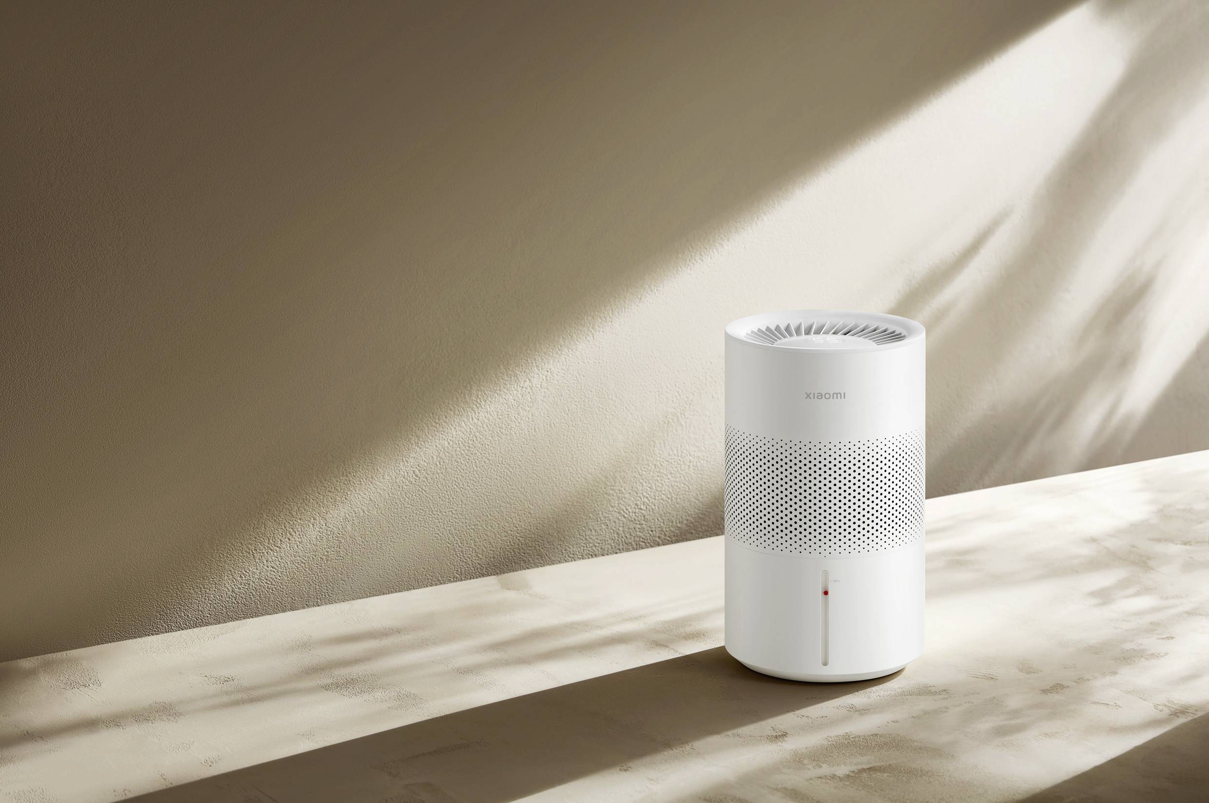 Ein moderner, weißer Luftreiniger steht auf einer Tischoberfläche. Sonnenlicht fällt von der Seite und erzeugt Schatten auf der Wand.
