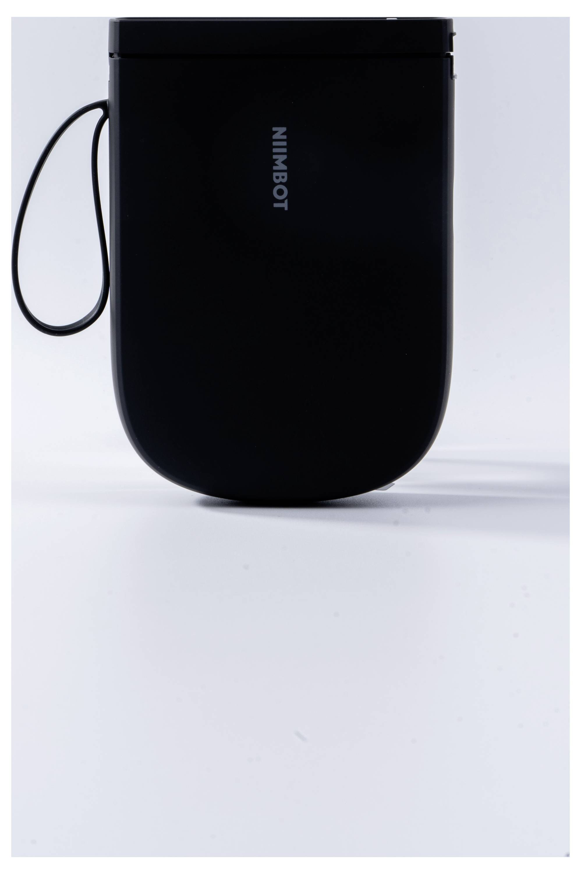 Ein schwarzes, abgerundetes Gerät mit dem Schriftzug 'NIMBOT' und einer seitlichen Schlaufe; es steht auf einer weißen Oberfläche.