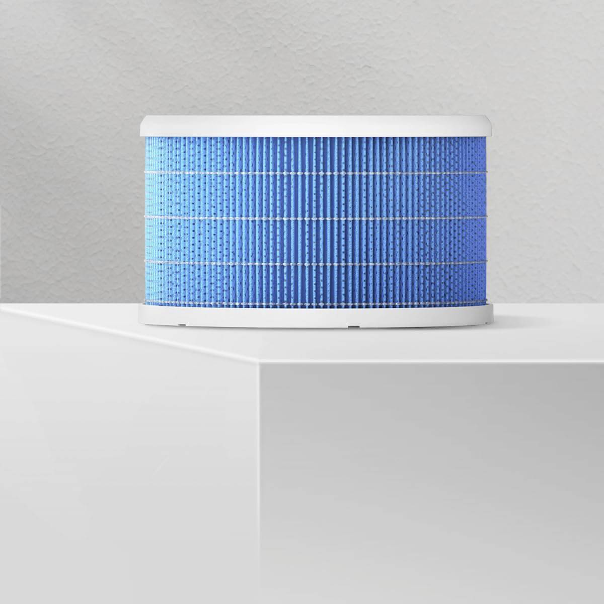 Ein runder blauer Luftfilter steht auf einem weißen Tisch vor einer grauen Wand. Ideal für die Luftreinigung im Innenbereich.