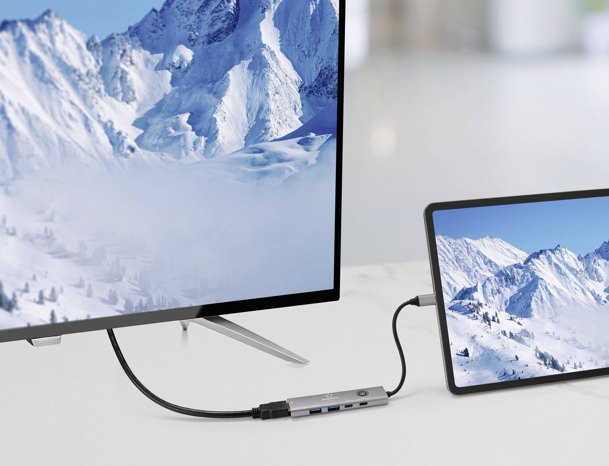 Ein Tablet ist mit einem großen Bildschirm verbunden, beide zeigen schneebedeckte Bergketten und veranschaulichen eine Bildschirmfreigabe-Einrichtung in einer modernen Umgebung.