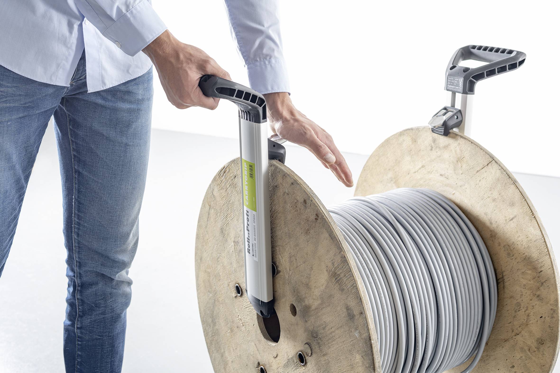 Eine Person hält einen Griff, der an einer großen Kabelspule angebracht ist. Die Spule ist aus Holz und enthält ein langes Kabel.