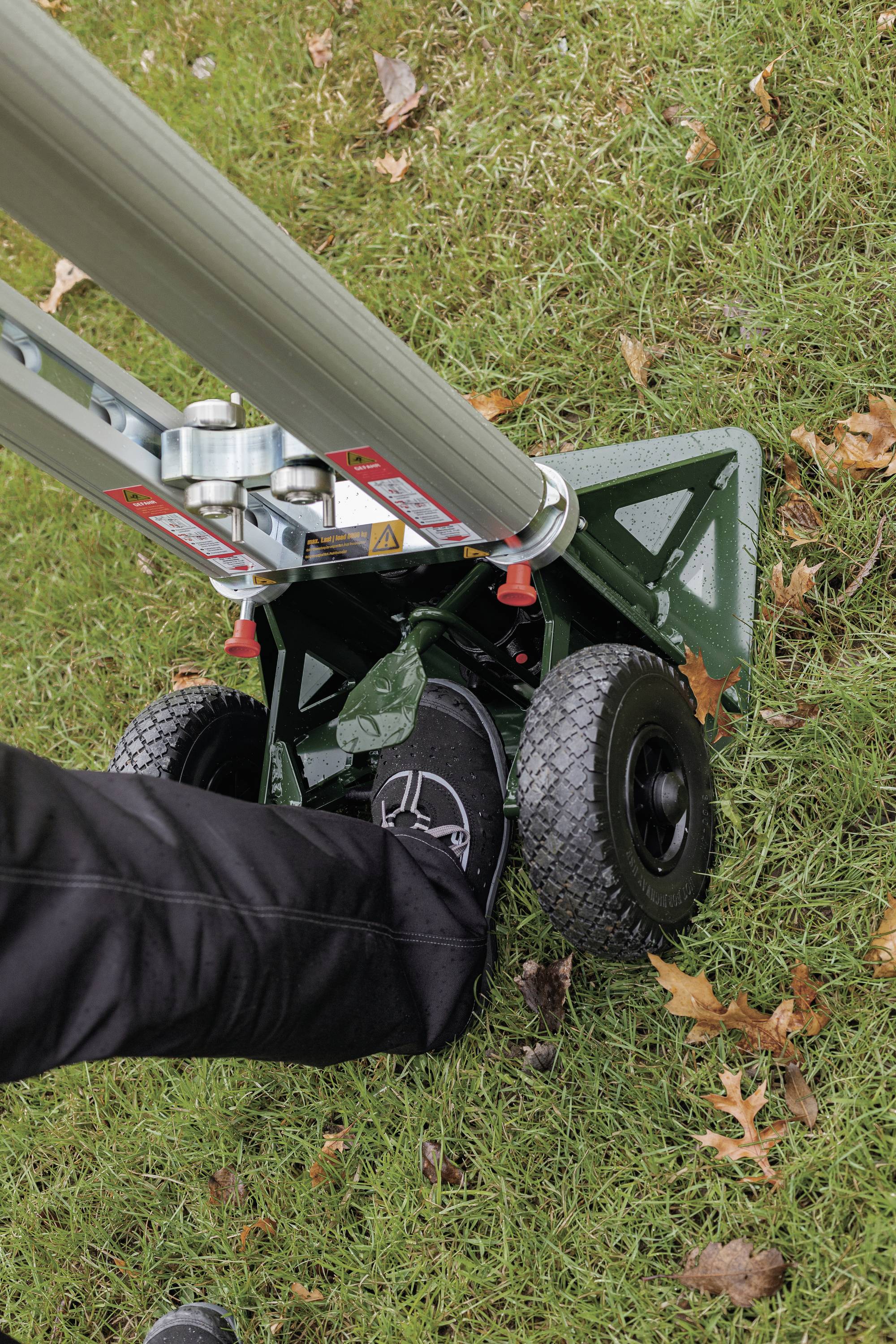 Eine Person drückt mit dem Fuß auf den Ständer eines tragbaren Mastsystems, das auf einer grasbewachsenen Fläche steht.