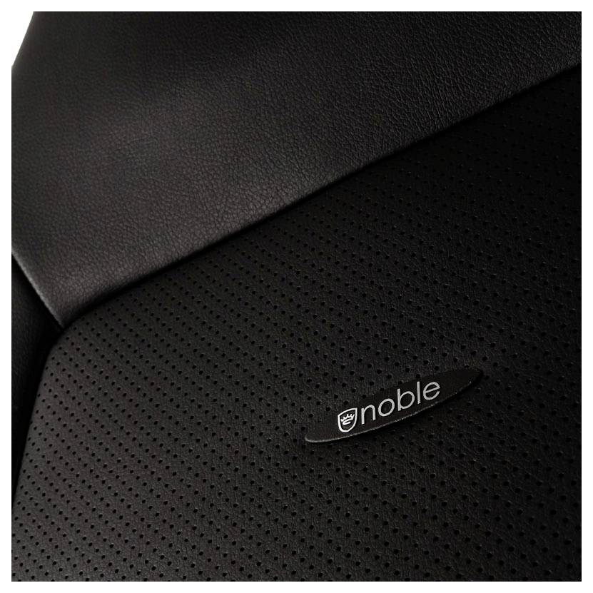 'Sitzfläche eines schwarzen Autositzes mit perforiertem Leder und einem ovalen Logo mit der Aufschrift 'noble'.'