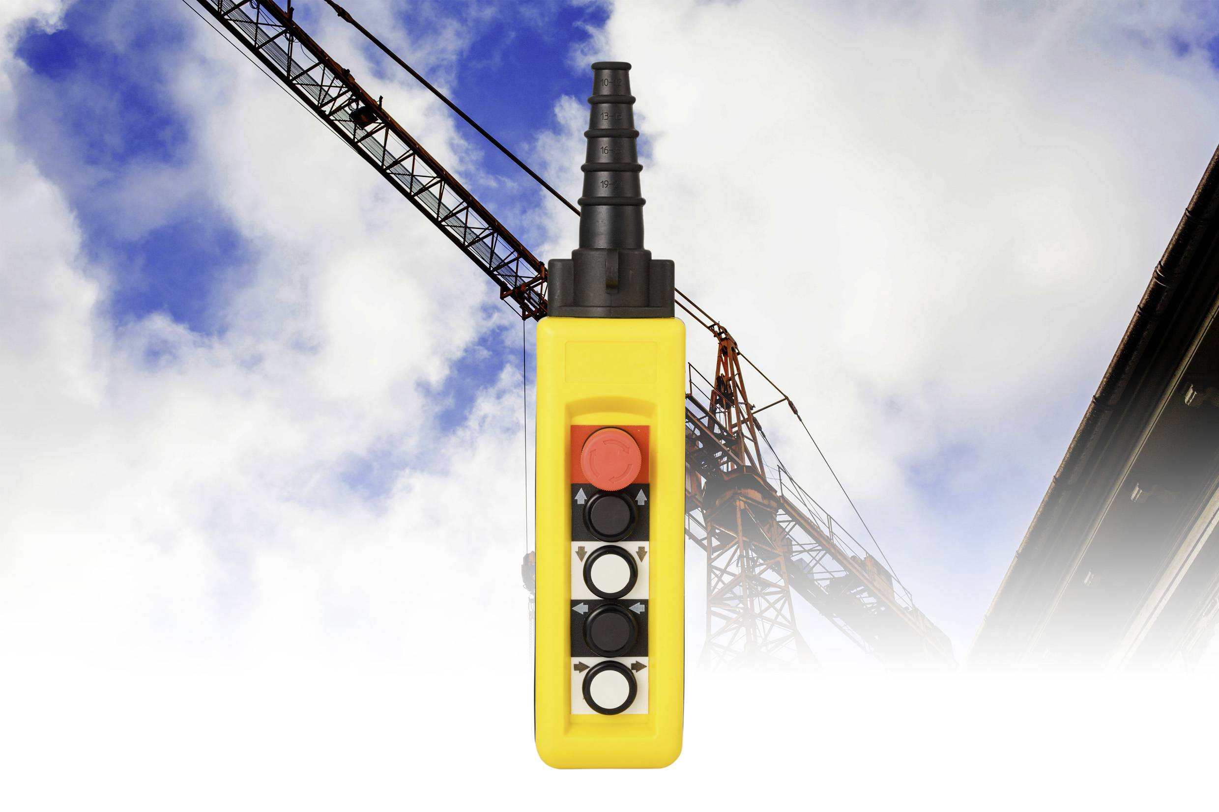 Ein gelbes Kransteuerungspanel mit vier Tasten, vor dem Hintergrund eines Baukrans und blauem Himmel mit Wolken.