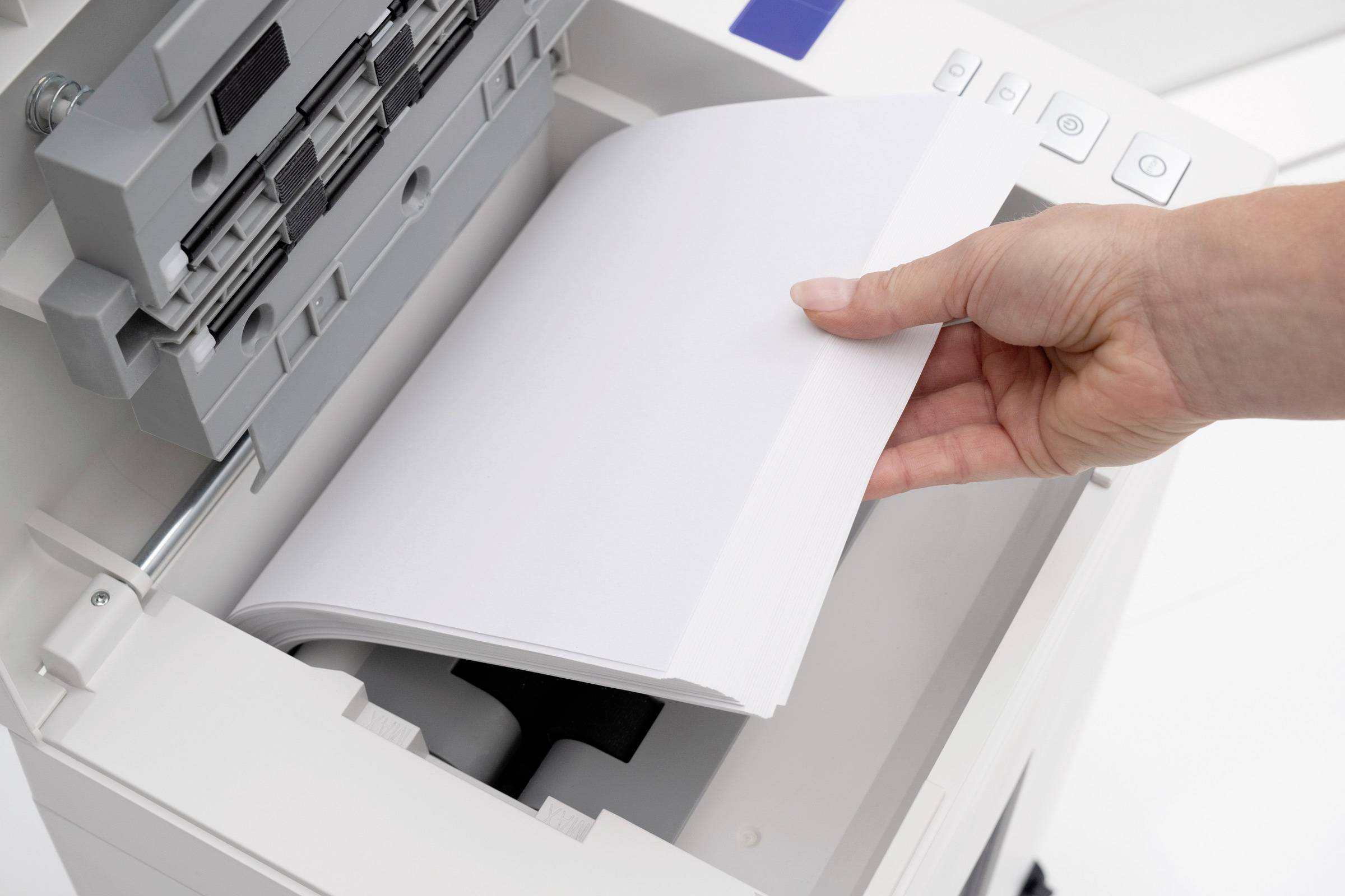 Eine Hand legt Papier in einen Drucker oder Kopierer ein. Das Bild zeigt den Einzugsschacht des Geräts und die vorbereiteten Blätter.