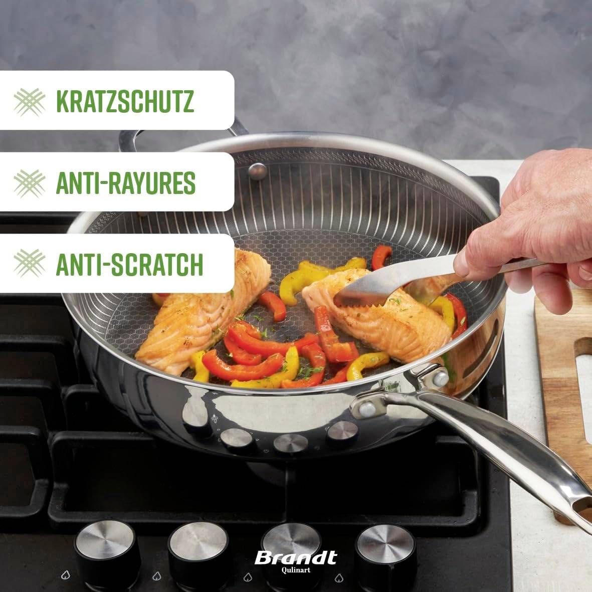 Pfanne auf Herd, gefüllt mit Lachs und Paprika. Text auf Bild: 'Kratzschutz', 'Anti-Rayures', 'Anti-Scratch'. Markiert Produktmerkmale.