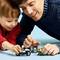 Ein Mann und ein Kind spielen mit einem Motorrad-Lego-Set auf einem blauen Tisch. Sie sind fröhlich und konzentriert.