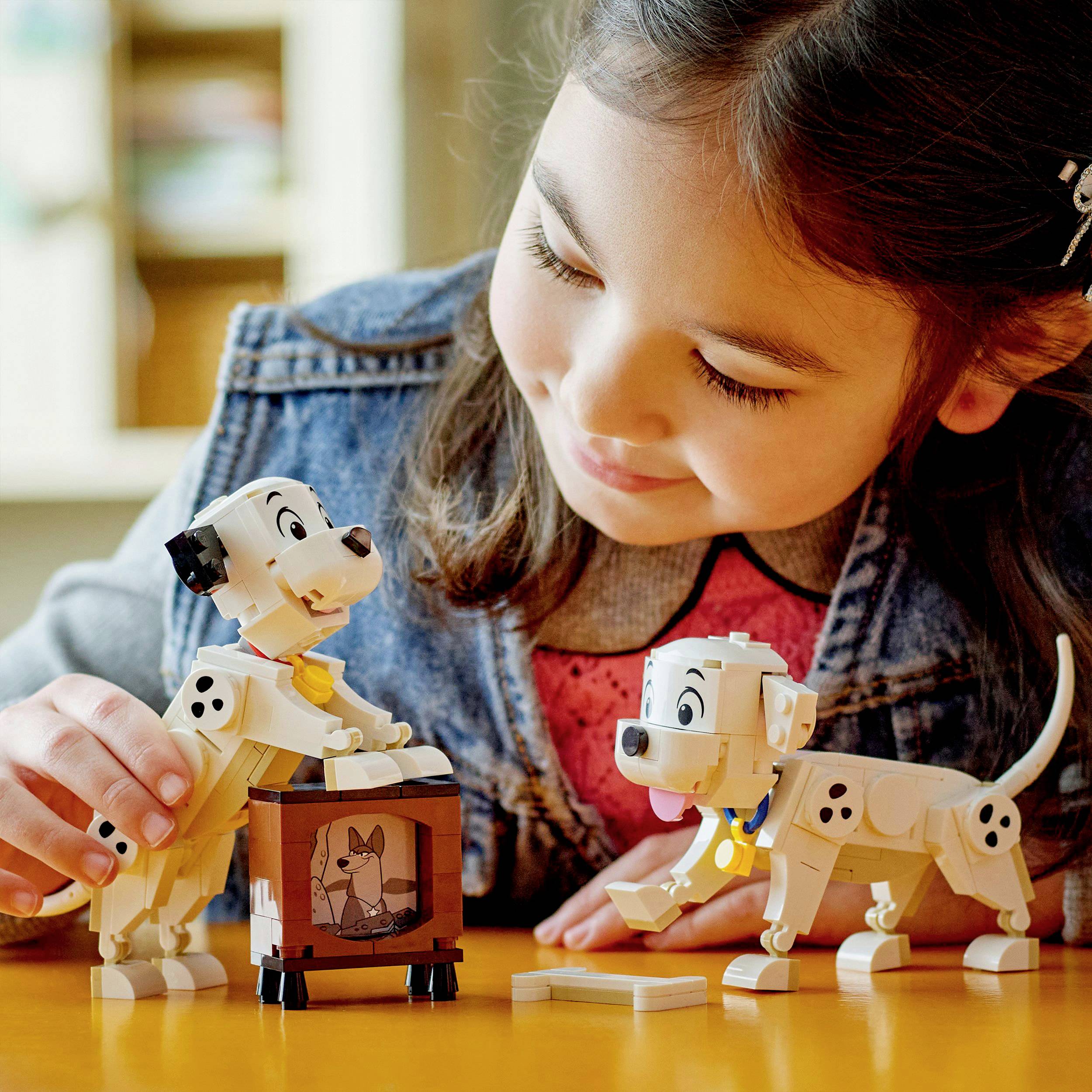 Ein Kind spielt lächelnd mit zwei Dalmatiner-Legofiguren auf einem Tisch.